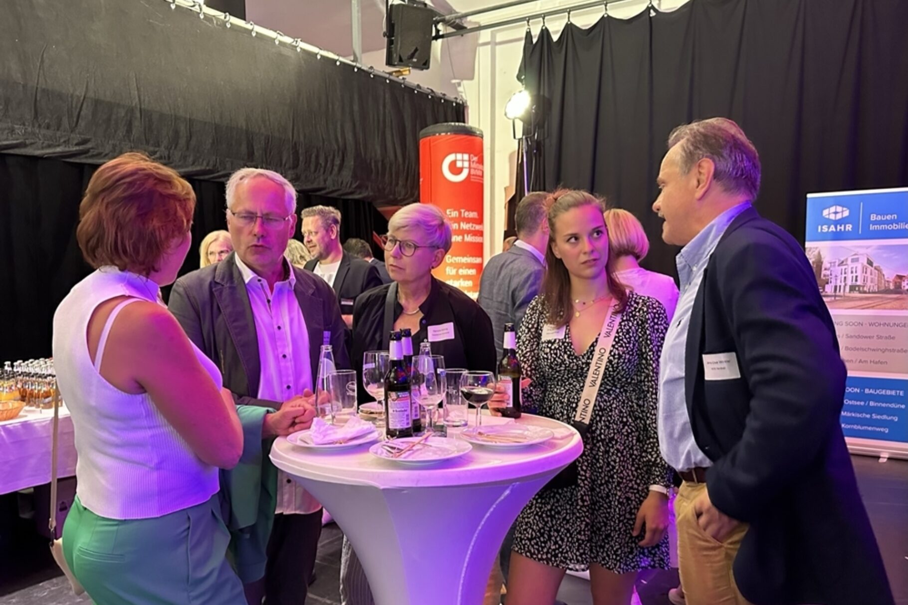 5 Menschen stehen um einem Stehtisch herum und unterhalten sich