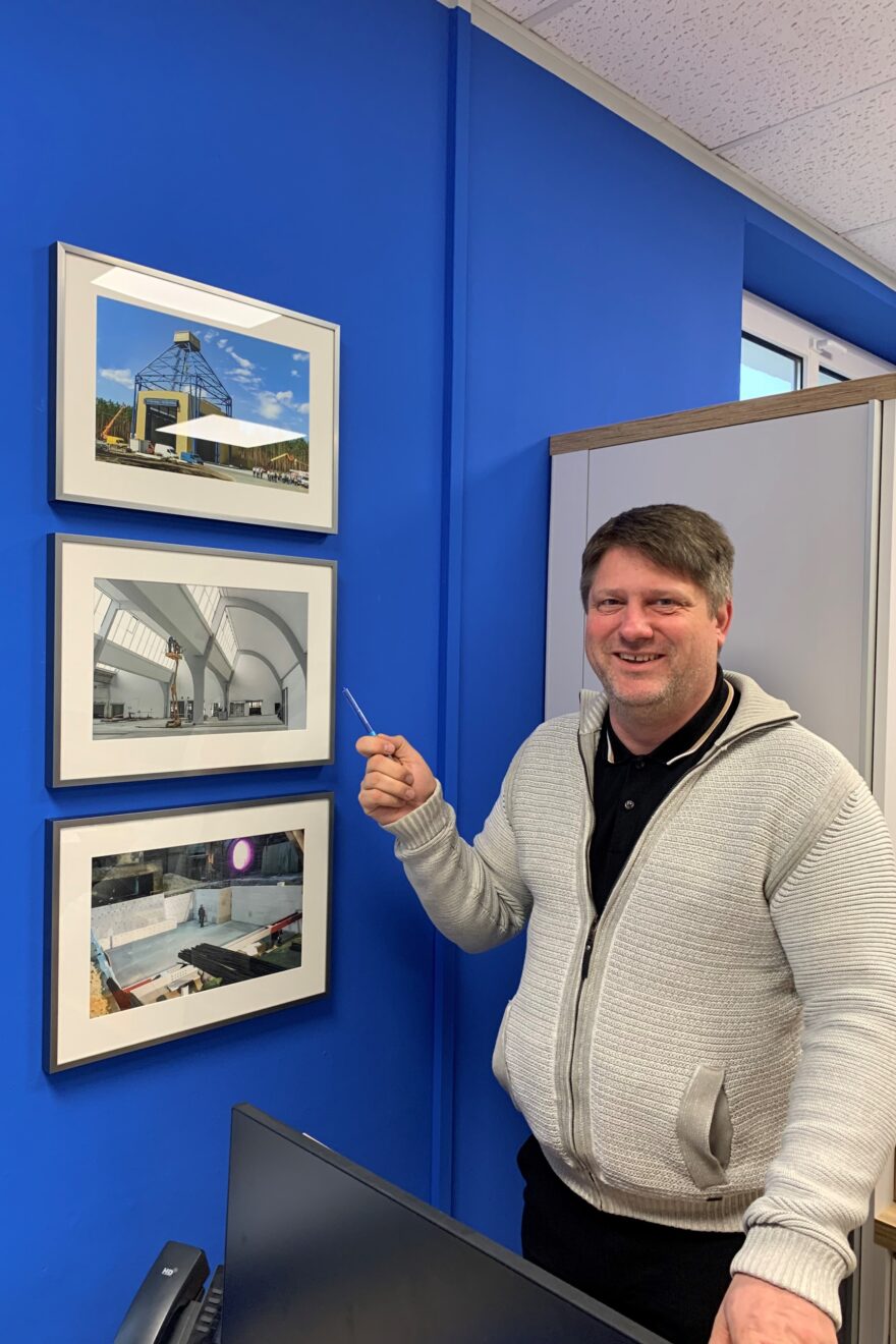 Mann zeigt auf Bilder an der Wand