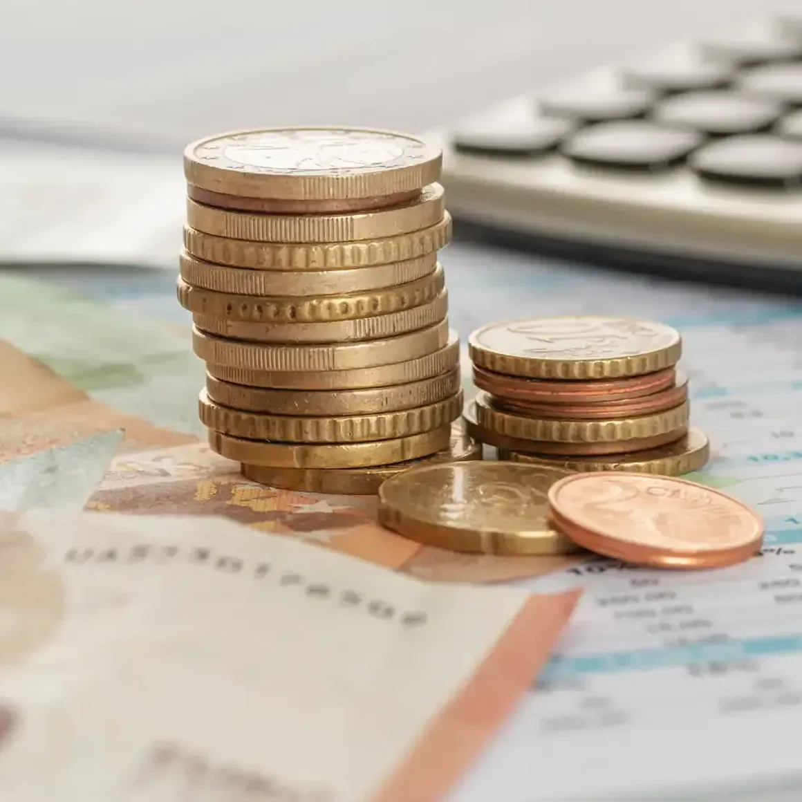 Ein Münzstapel liegt auf einem Schreibtisch neben einem Taschenrechner und einem Kugelschreiber