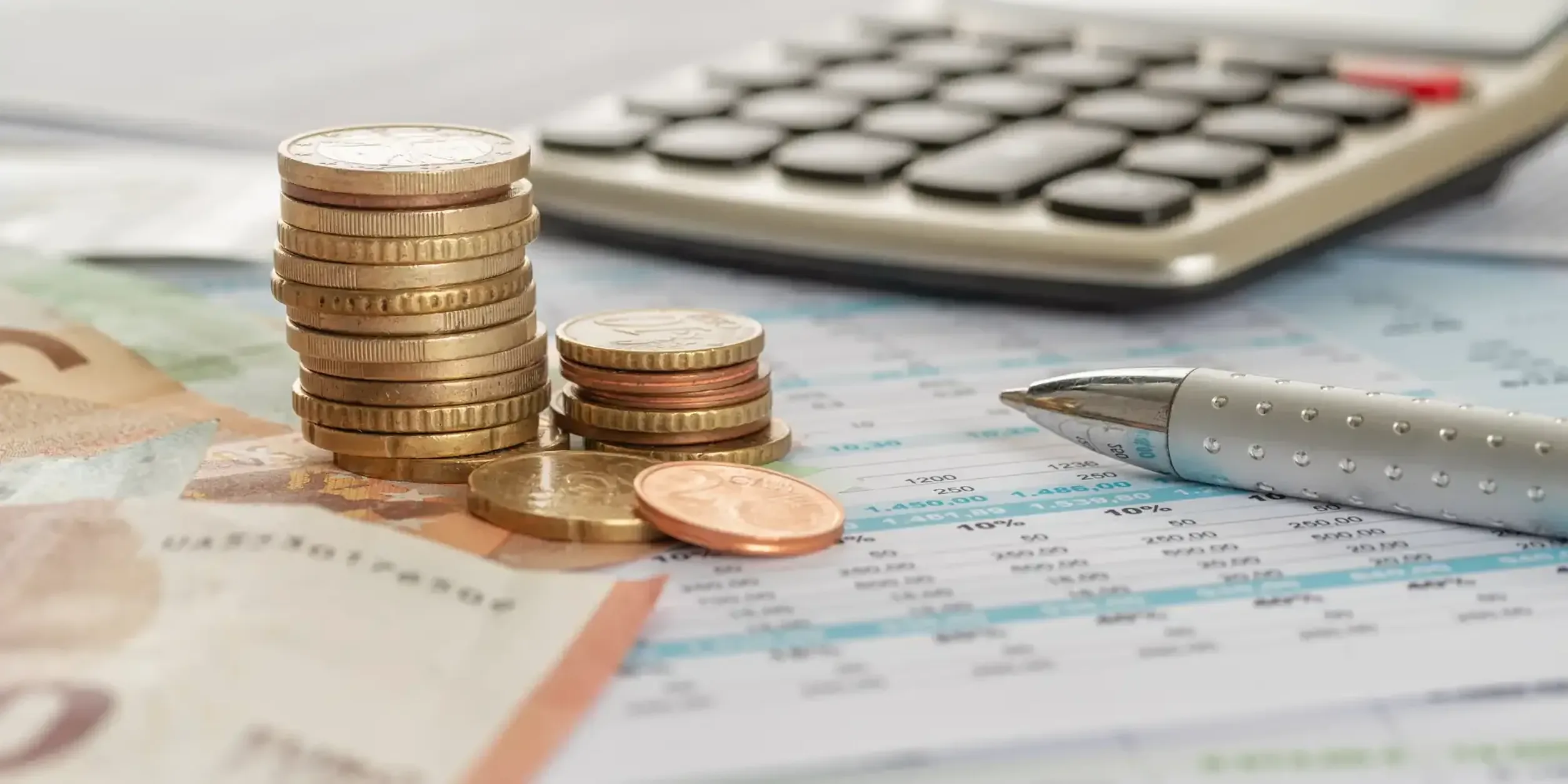 Ein Münzstapel liegt auf einem Schreibtisch neben einem Taschenrechner und einem Kugelschreiber