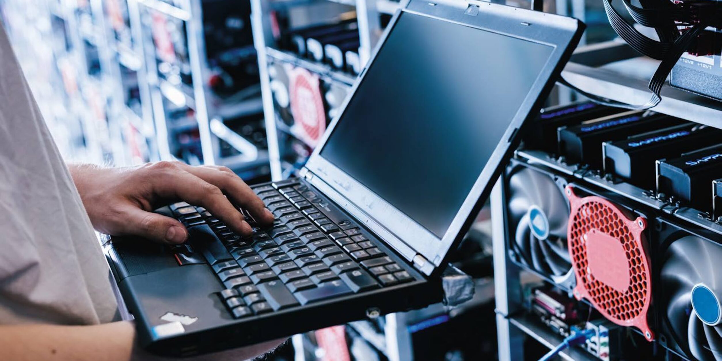 Eine Person hält einen geöffneten Laptop vor einem Großrechnern in der Hand