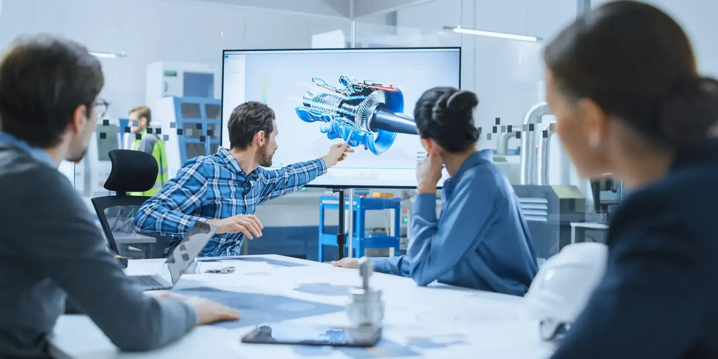 Mehrere Personen sitzen in einer Besprechung zusammen und schauen auf einen Bildschirm