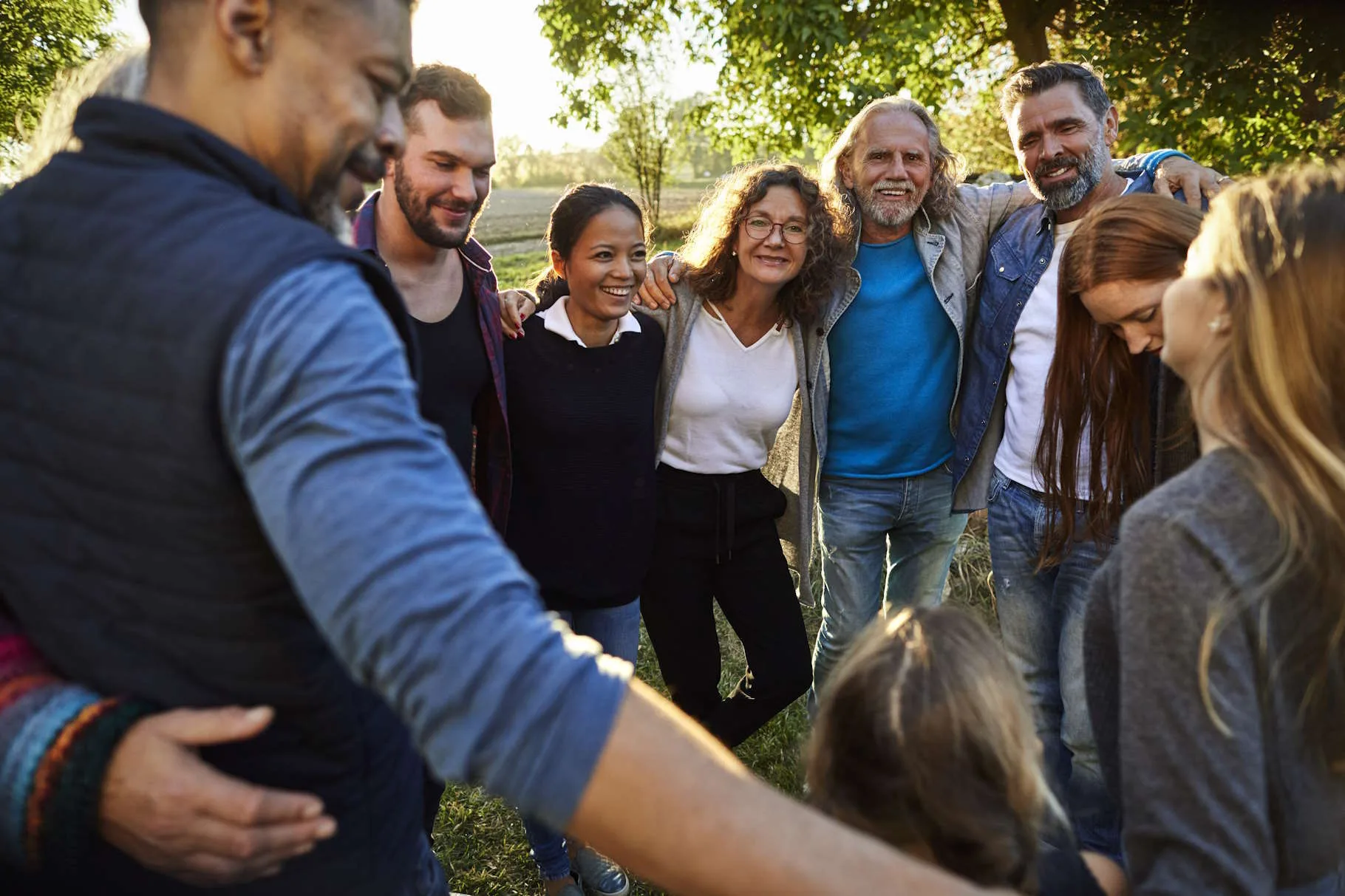 Mehrere Personen stehen, die Arme über die Schulter des anderen gelegt, im Kreis zusammen