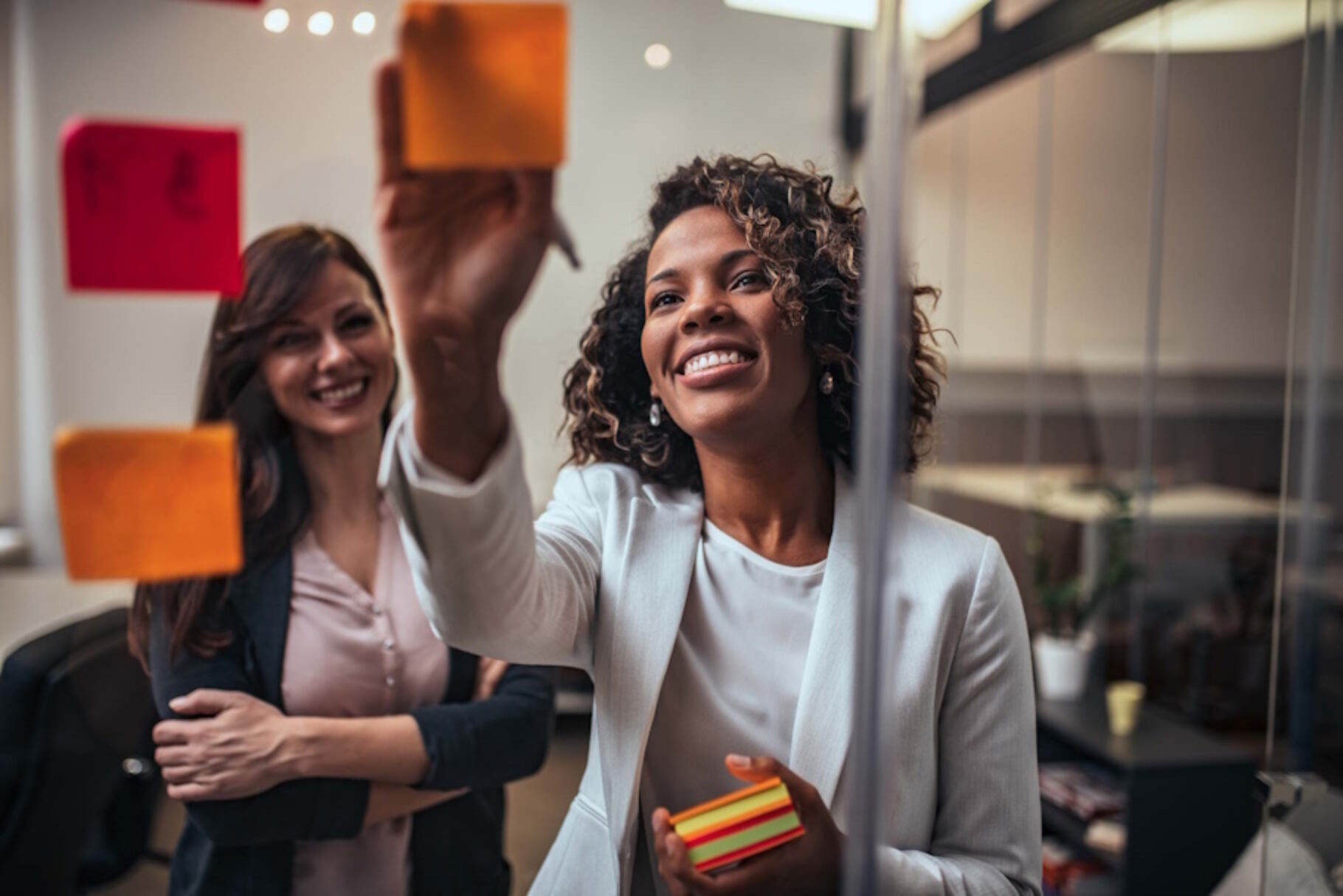 2 Personen schauen auf eine Glaswand und bekleben diese mit beschriebenen Haftnotizen