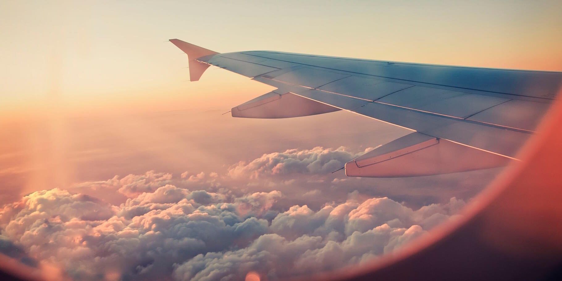 Blick aus einem Flugzeugfenster nach draußen auf die Tragflächen mit Sonnenuntergang im HIntergrund