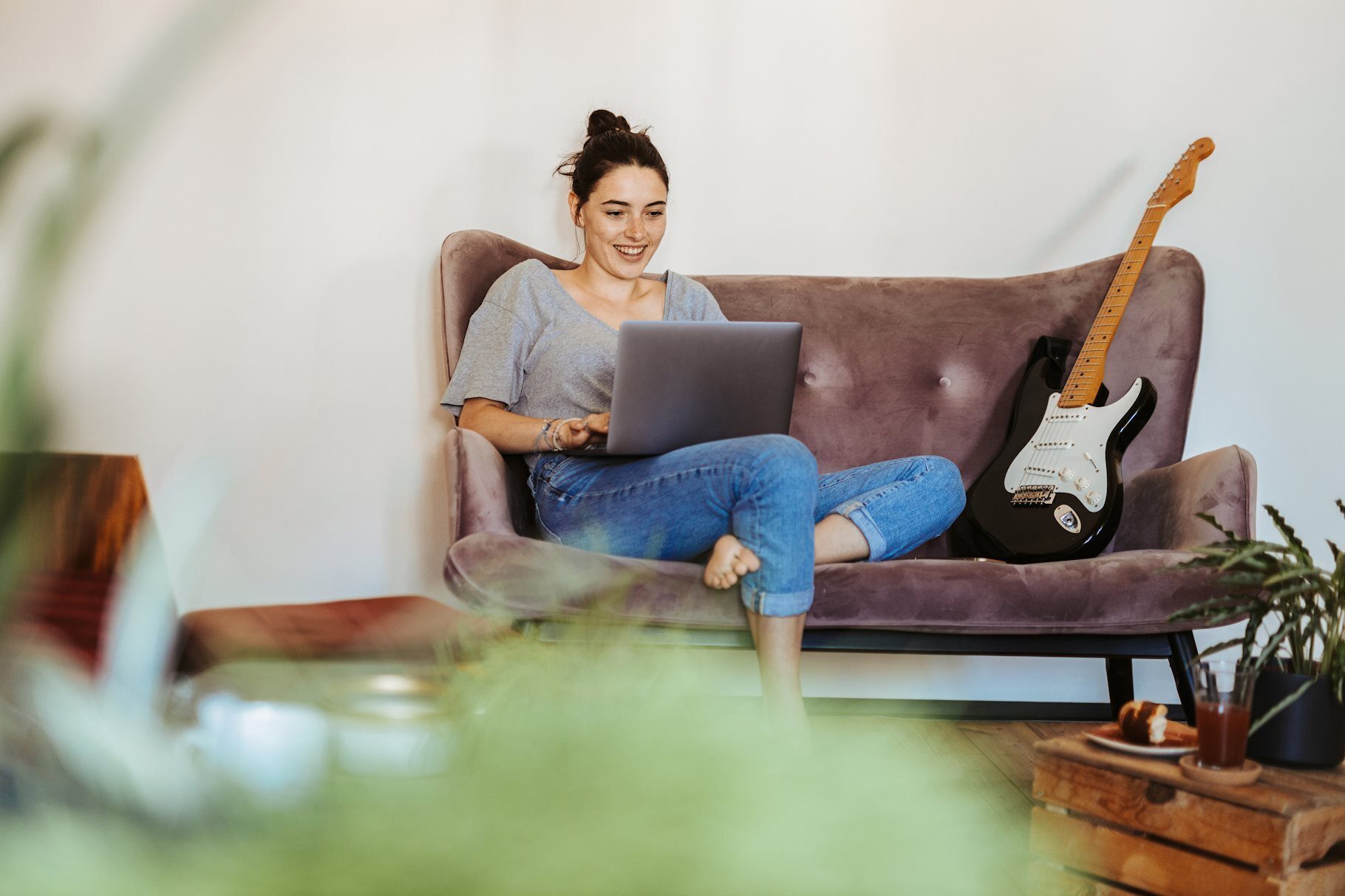 Eine Frau sitzt mit einem Laptop gemütlich auf dem Sofa