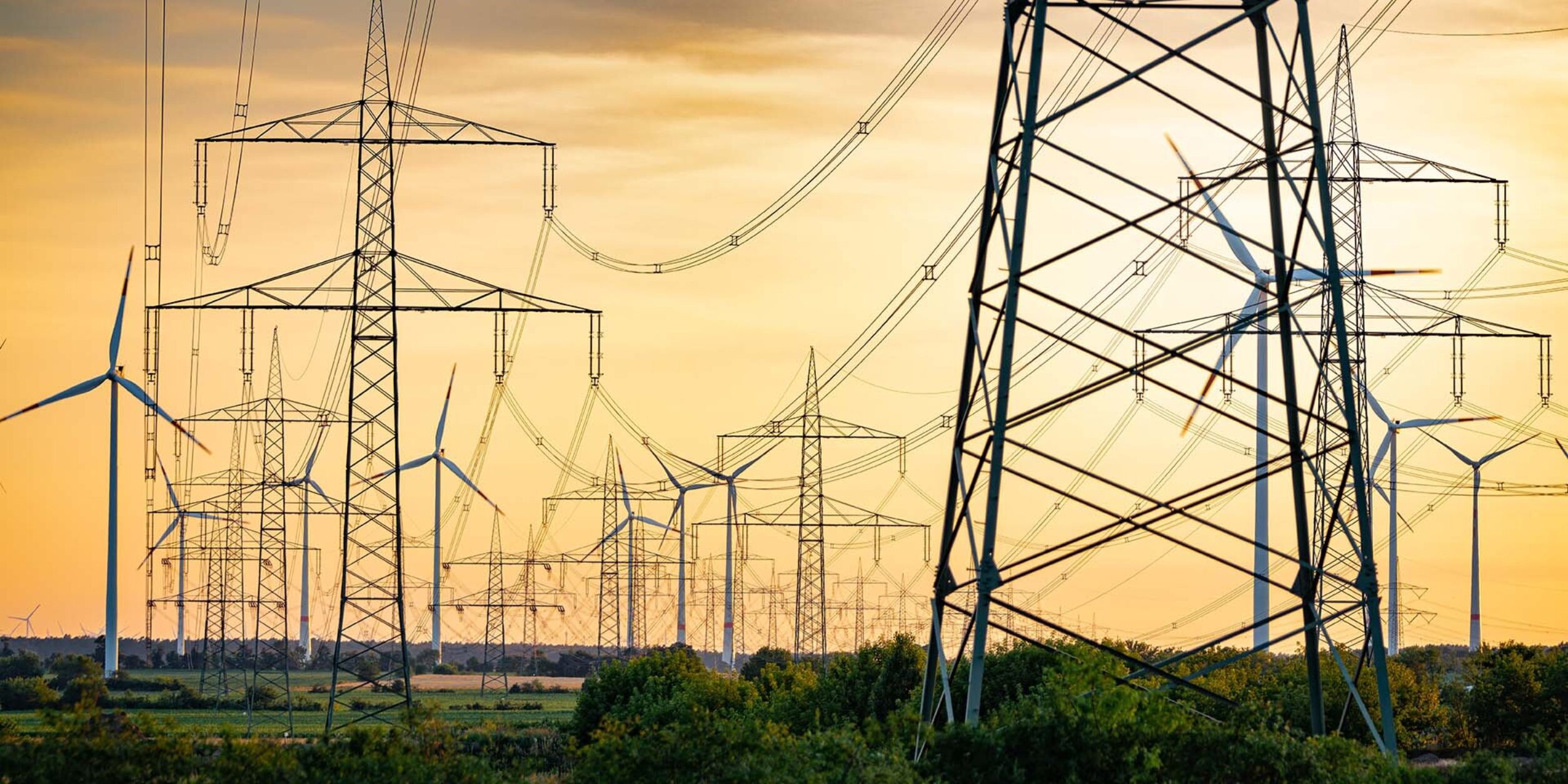 Hochspannungsleitungen und Windräder im Sonnenuntergang