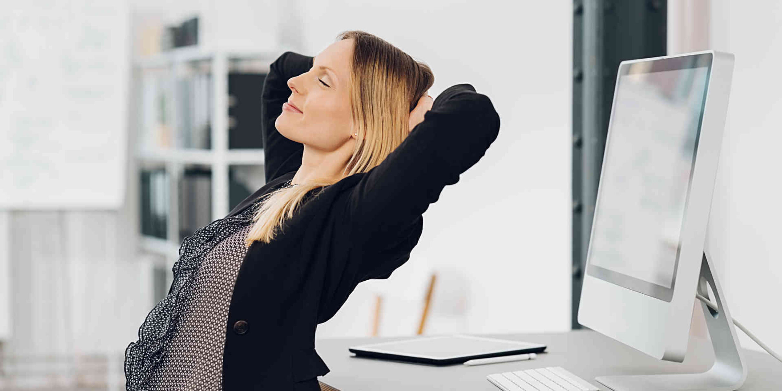 Eine Frau lehnt sich entspannend am Arbeitsplatz zurück