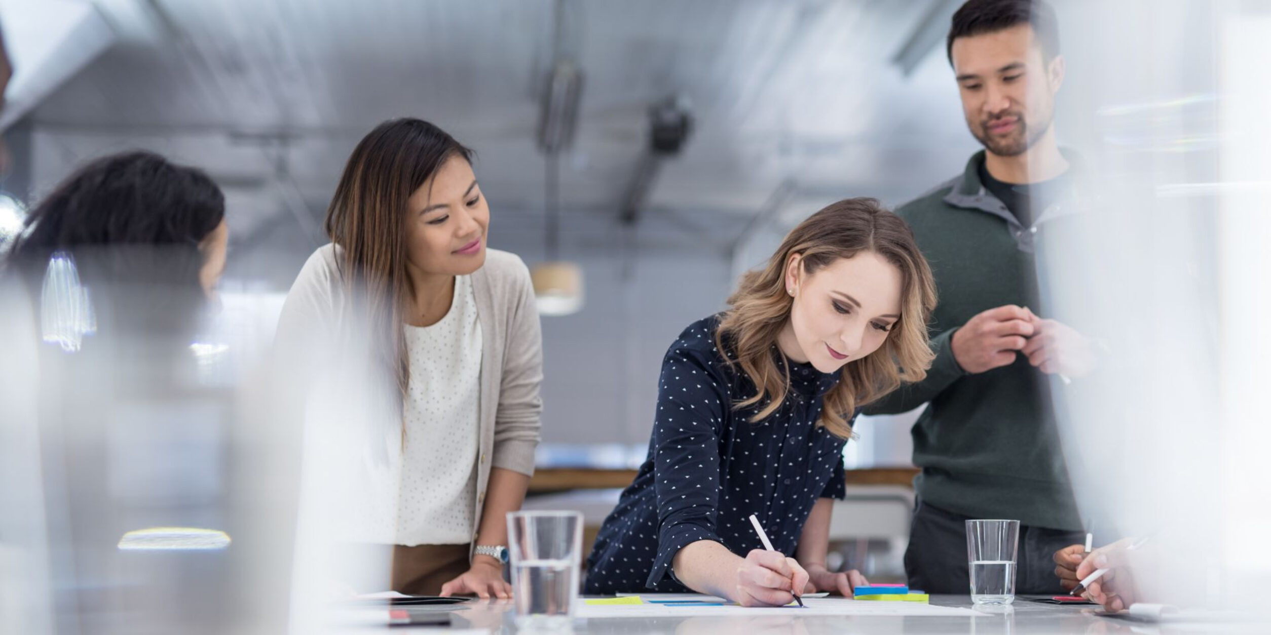 4 Personen stehen um einen Tisch während eine Person schreibt