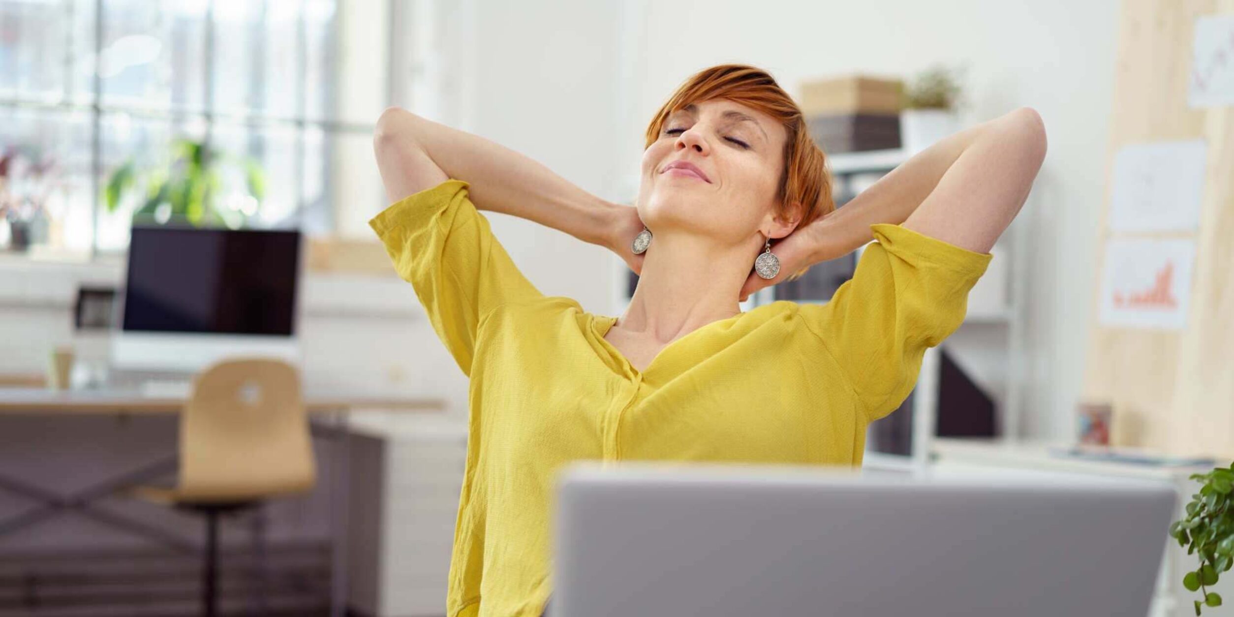 Eine vor dem Laptop sitzende Frau lehnt sich im Stuhl entspannt zurück