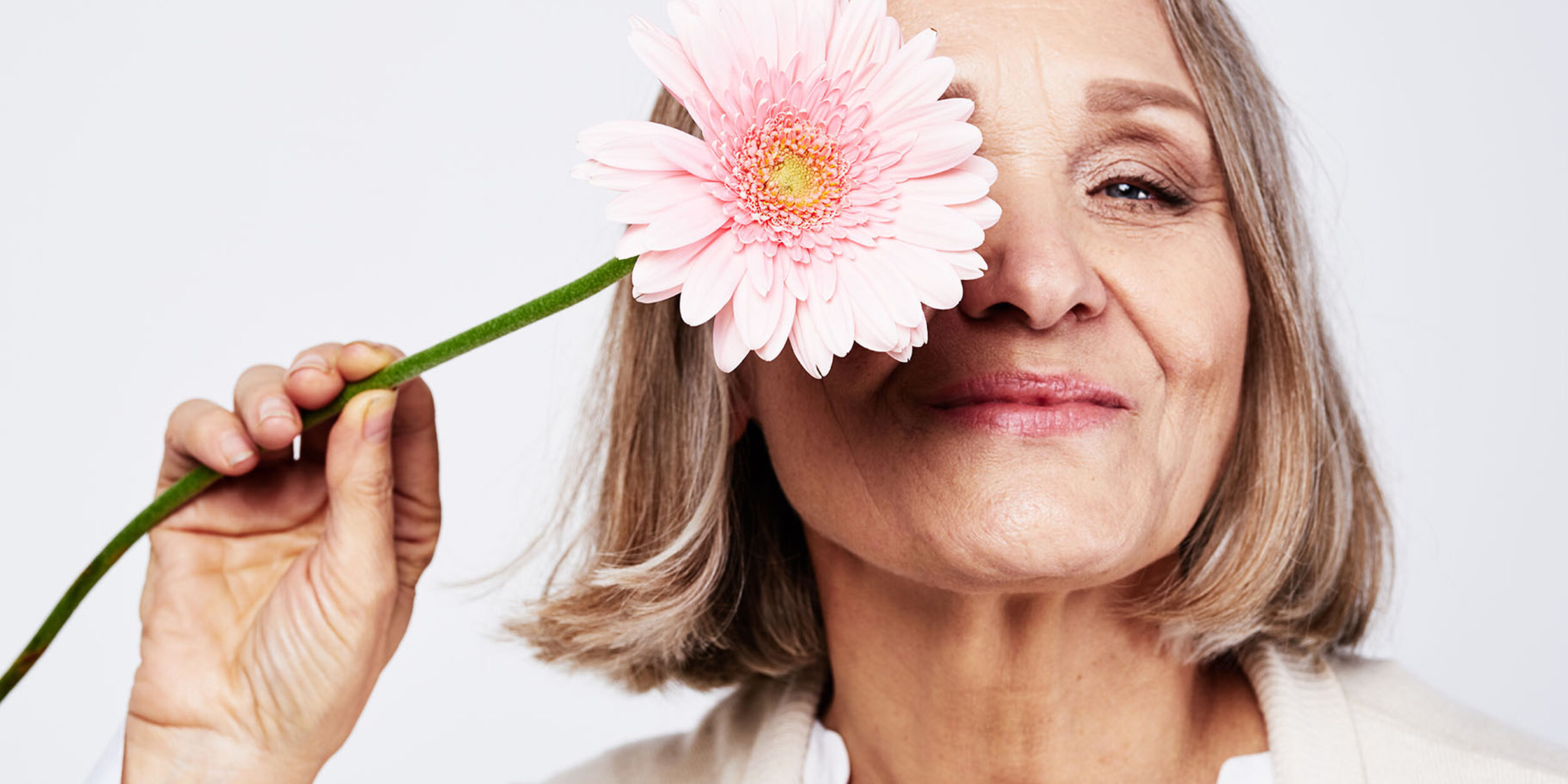 Eine Frau hält sich die Blüte einer Blume vor ihr eines Auge.