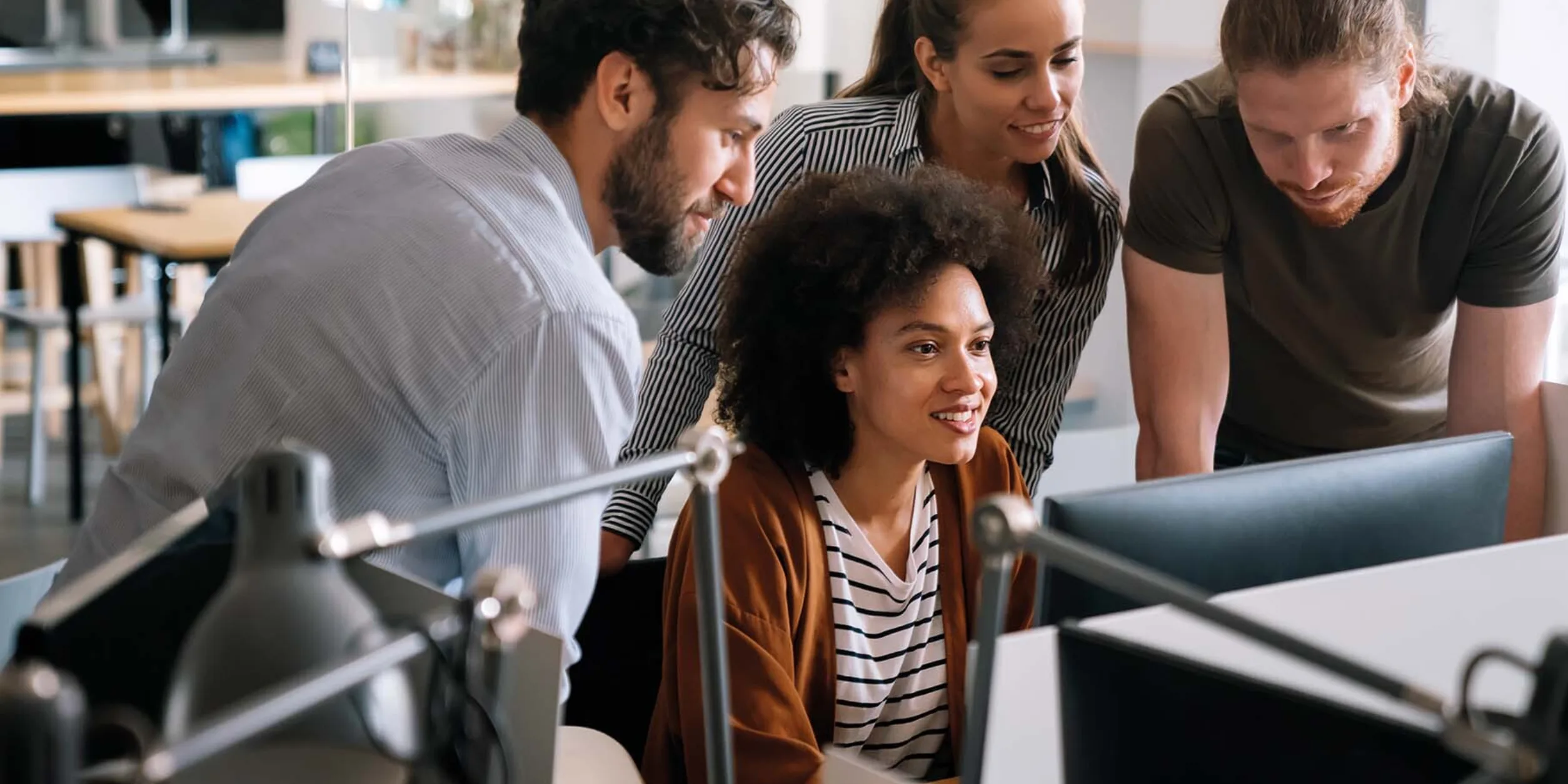 Mitarbeiter:innen gemeinsam im Büro an einem PC-Arbeitsplatz