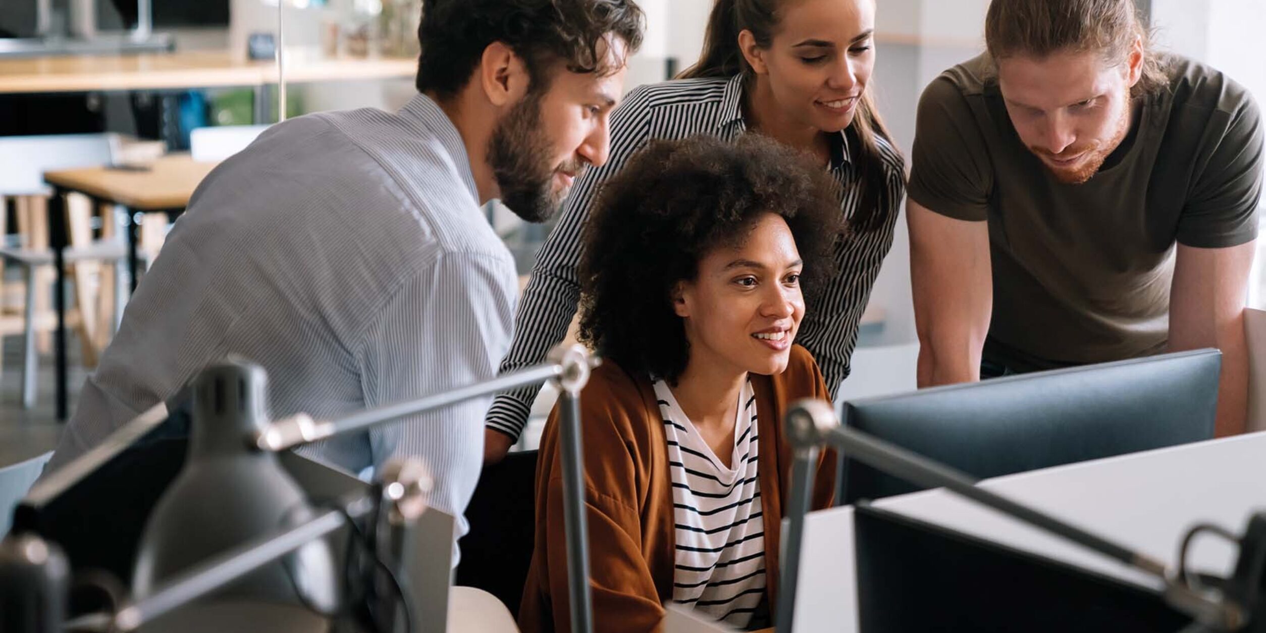 Mitarbeiter:innen gemeinsam im Büro an einem PC-Arbeitsplatz