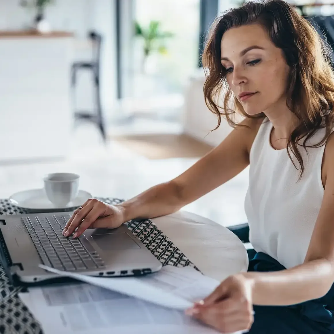 Geschäftsfrau sitzt in der Küche am Tisch und arbeitet am Laptop