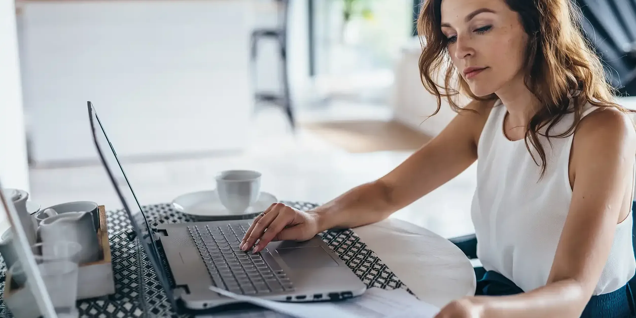 Geschäftsfrau sitzt in der Küche am Tisch und arbeitet am Laptop