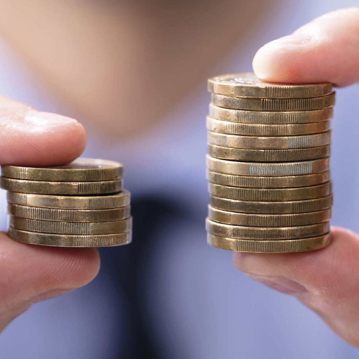 2 Münzstapel werden jeweils zwischen 2 Fingern von einer Person gehalten und in die Kamera gezeigt