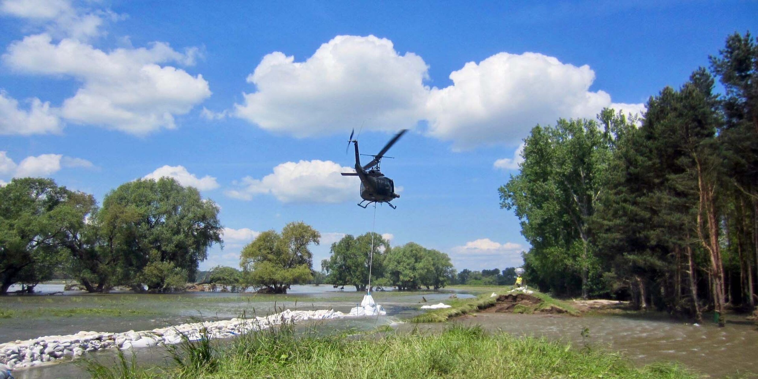 Ein Hubschrauber seilt einen Sandsack an einer Hochwasserbarriere ab.