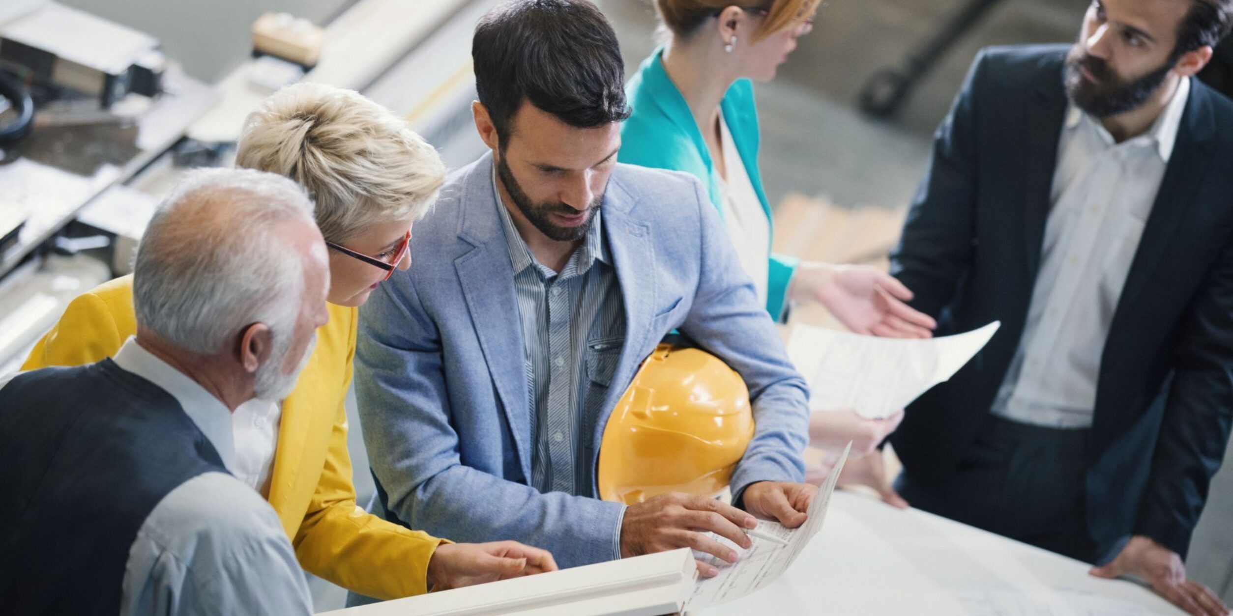 Drei Personen in Businesskleidung besprechen einen Plan auf einer Baustelle