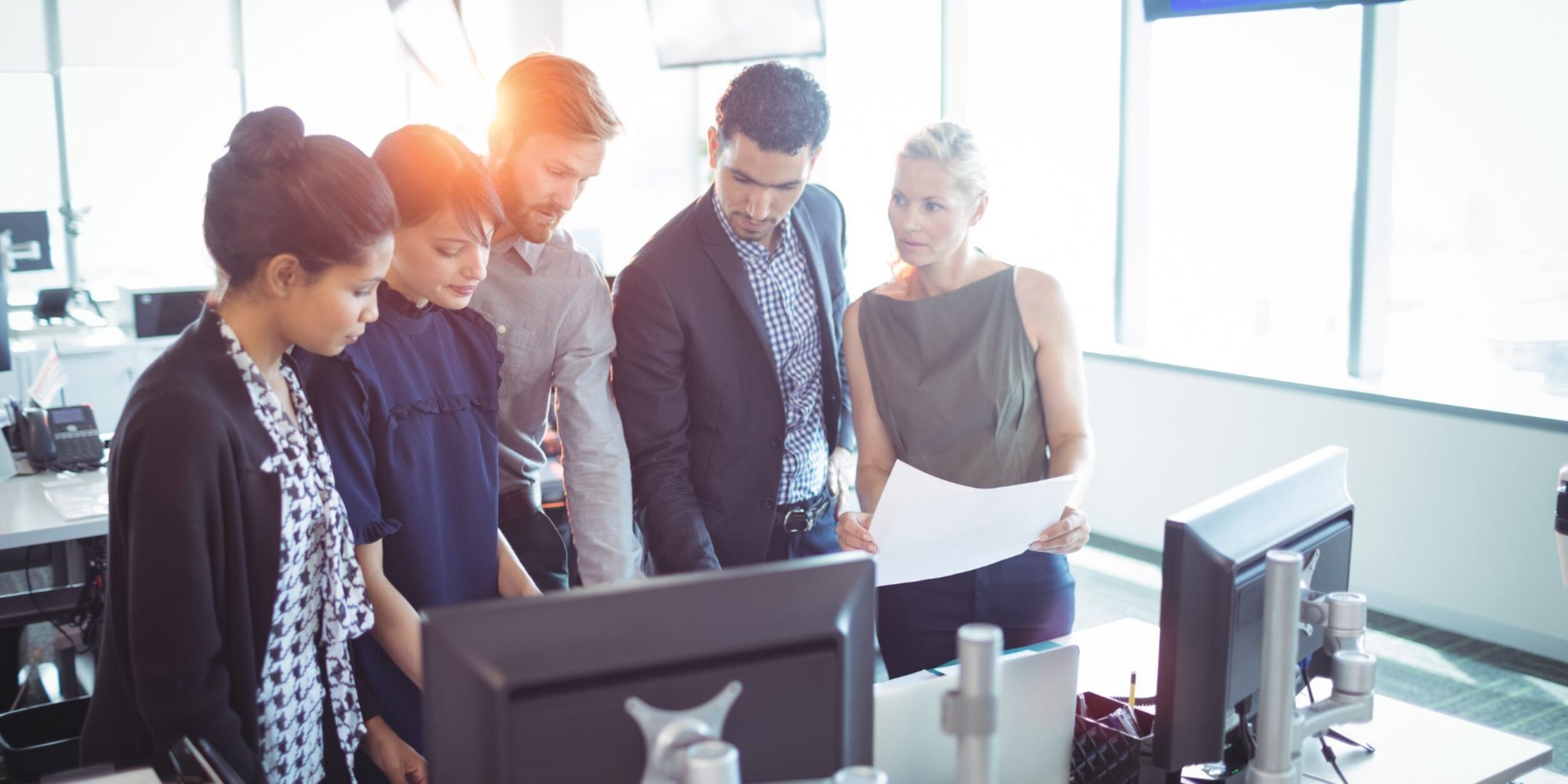 Mehrere Personen schauen besorgt auf Dokumente, die auf einem Schreibtisch vor einem Bildschirm liegen.