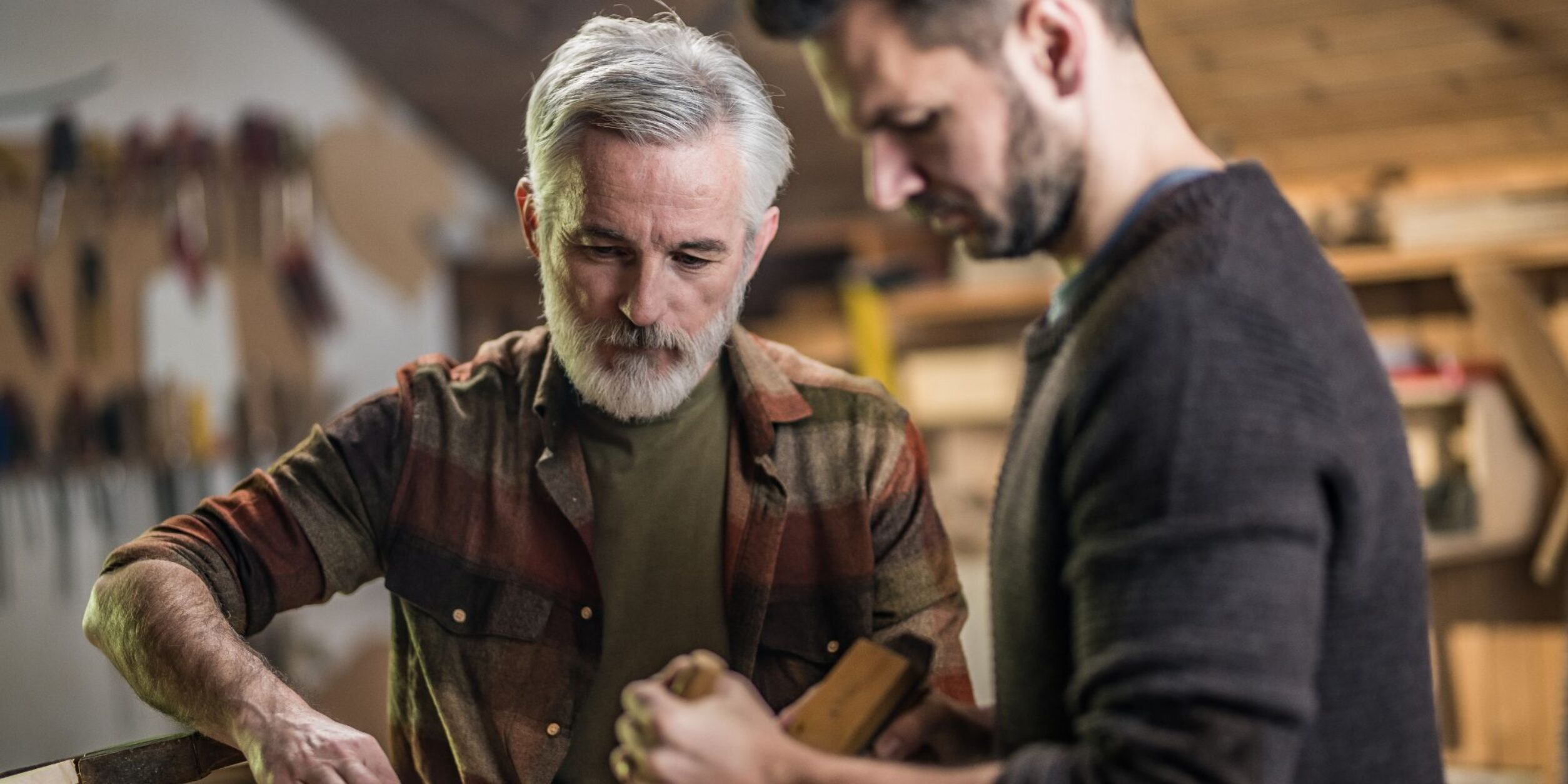 Ein älterer Mann nimmt mit einem jungen Mann Tischlerarbeiten vor.