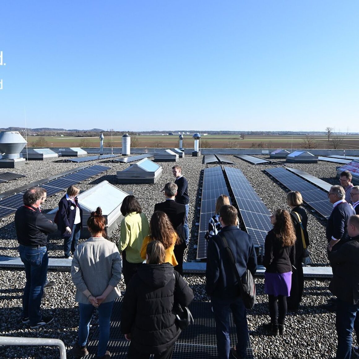 Menschen stehen auf Flachdach mit Solarkollektoren, Logo BVMW e.V., Logo Energieagentur Ebersberg