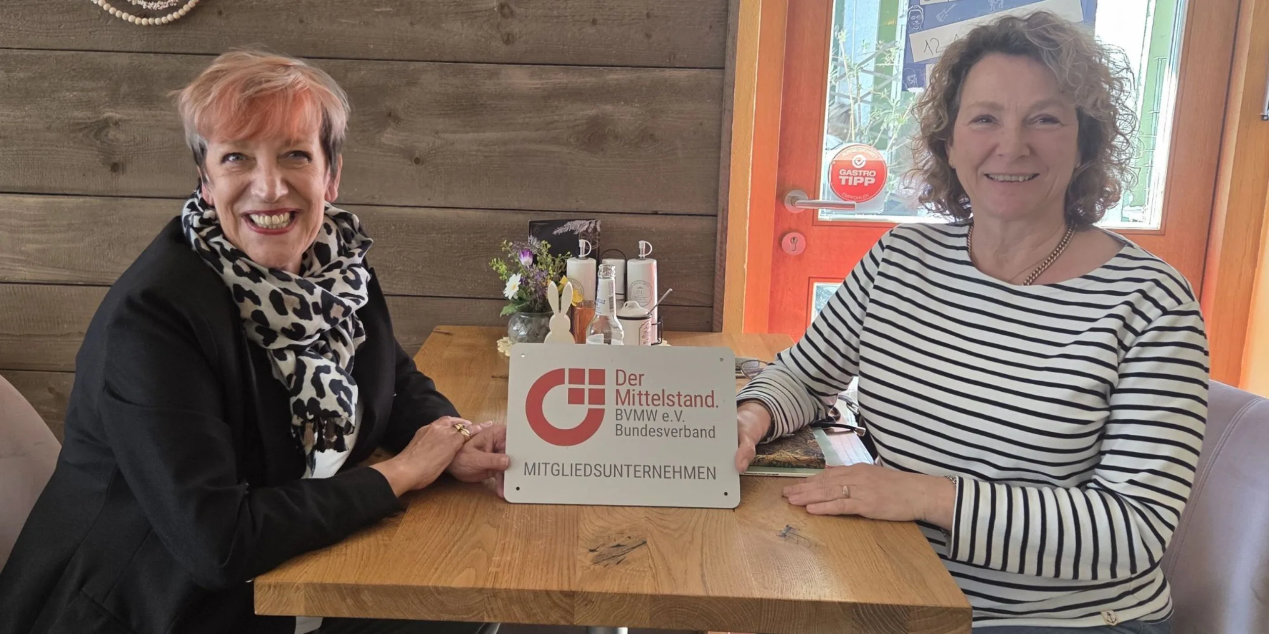 C. Matheja, Dr. Schulze-Moews an Tisch sitzend mit BVMW Mitgliedsunternehmen Plakette