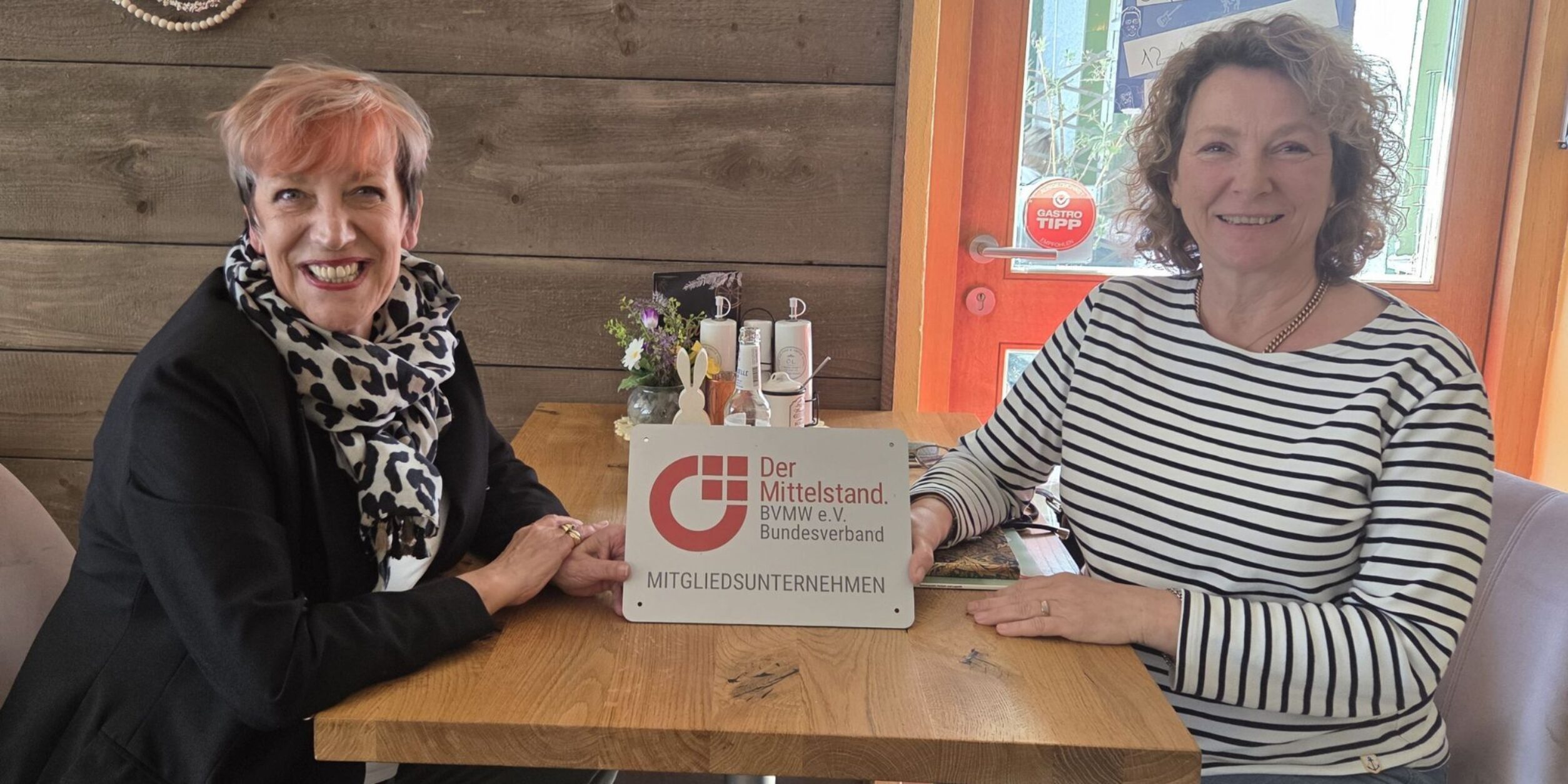 C. Matheja, Dr. Schulze-Moews an Tisch sitzend mit BVMW Mitgliedsunternehmen Plakette