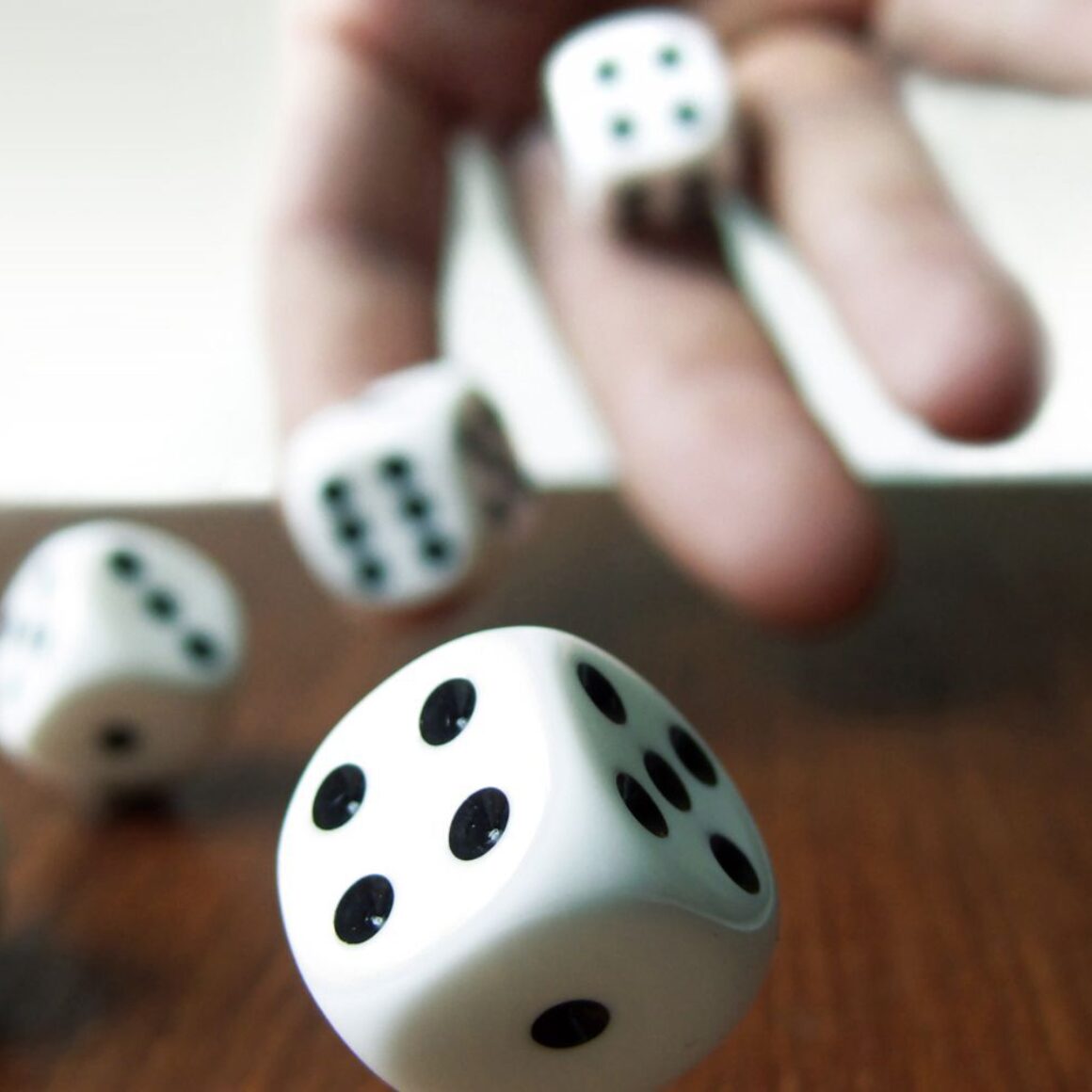 Hand würfelt 5 Würfel über braunen Holztisch, Logo BVMW