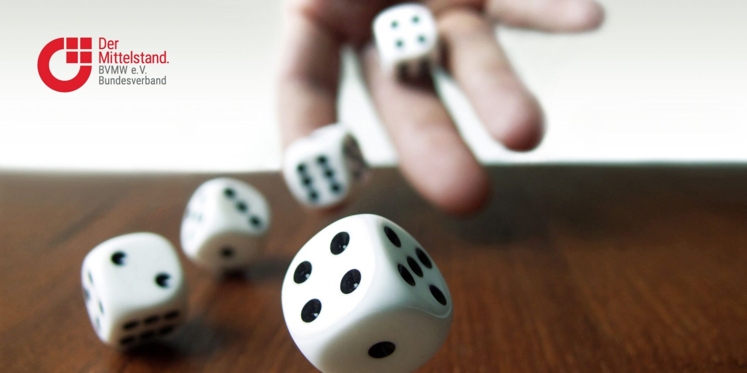 Hand würfelt 5 Würfel über braunen Holztisch, Logo BVMW