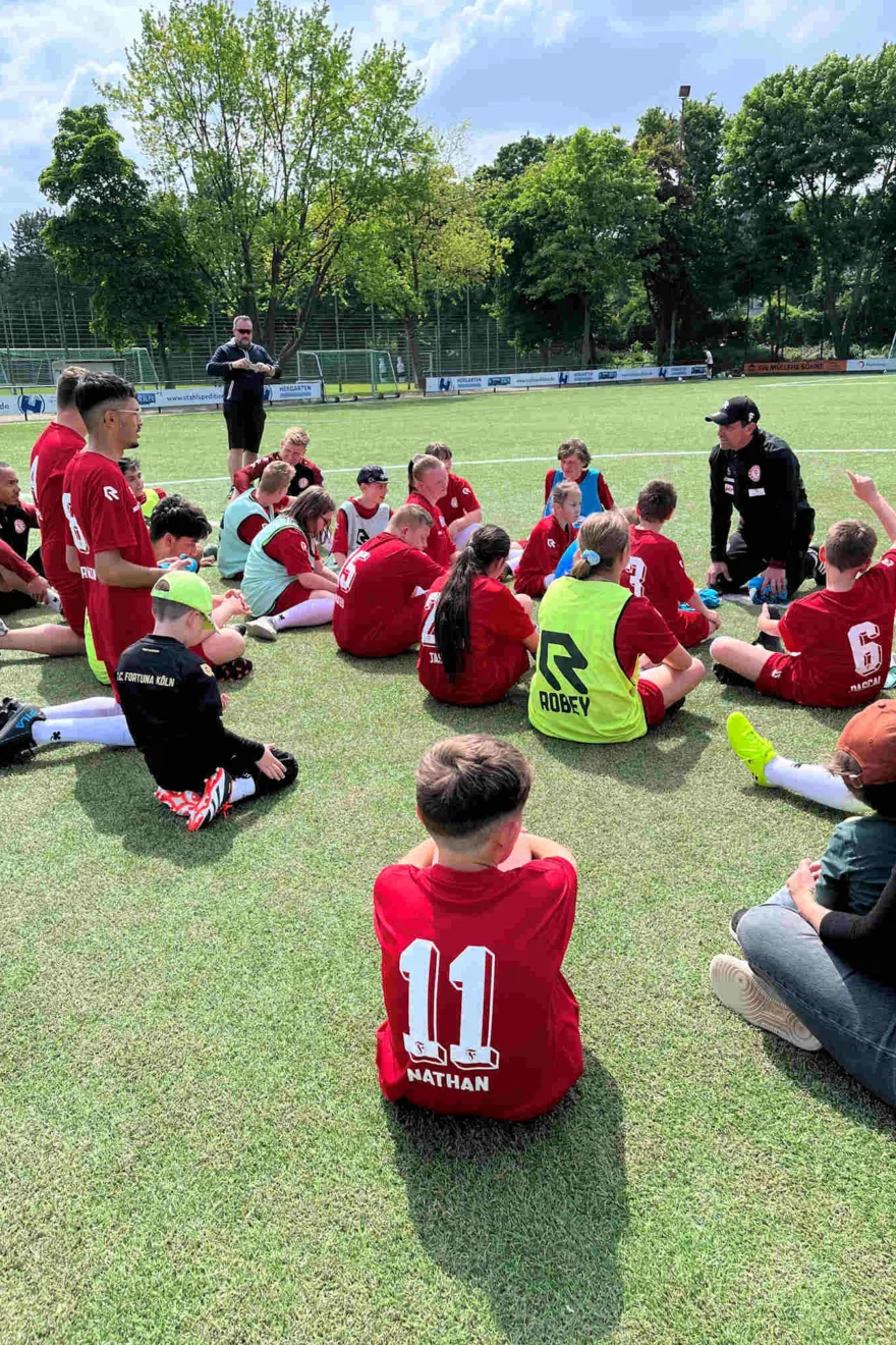 Kinder sitzen auf dem Rasen und hören Trainer zu