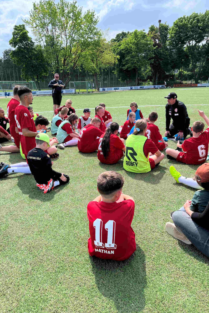Kinder sitzen auf dem Rasen und hören Trainer zu