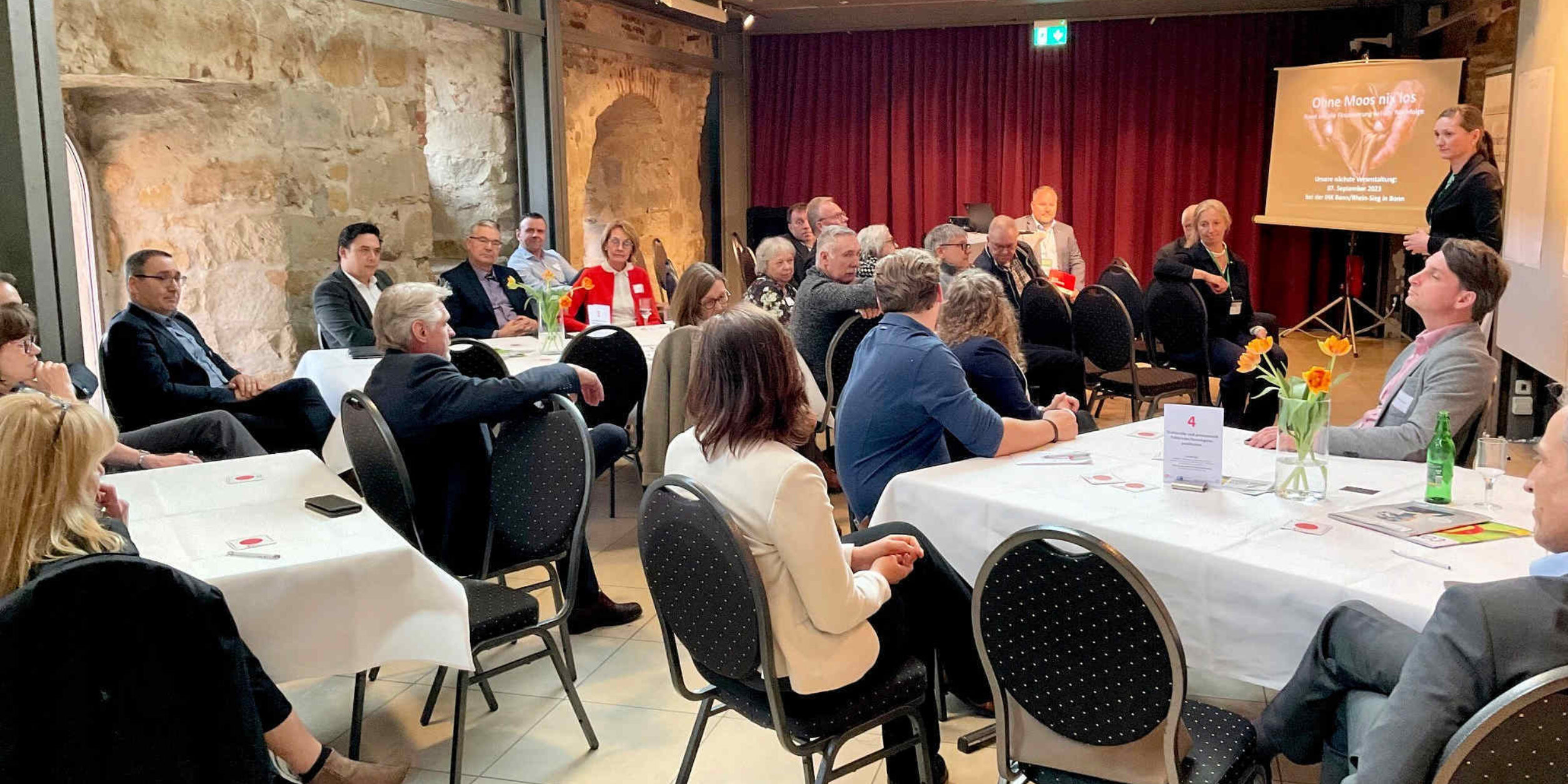 Teilnehmer an den Tischen hören dem Vortrag zu