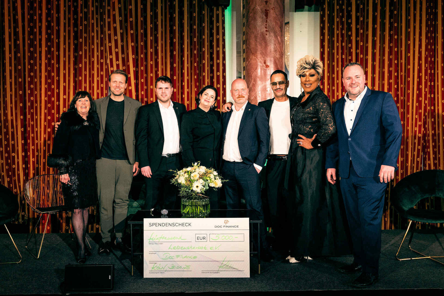 Organisatoren, Referenten und Moderatorin auf der Bühne mit Spendenscheck