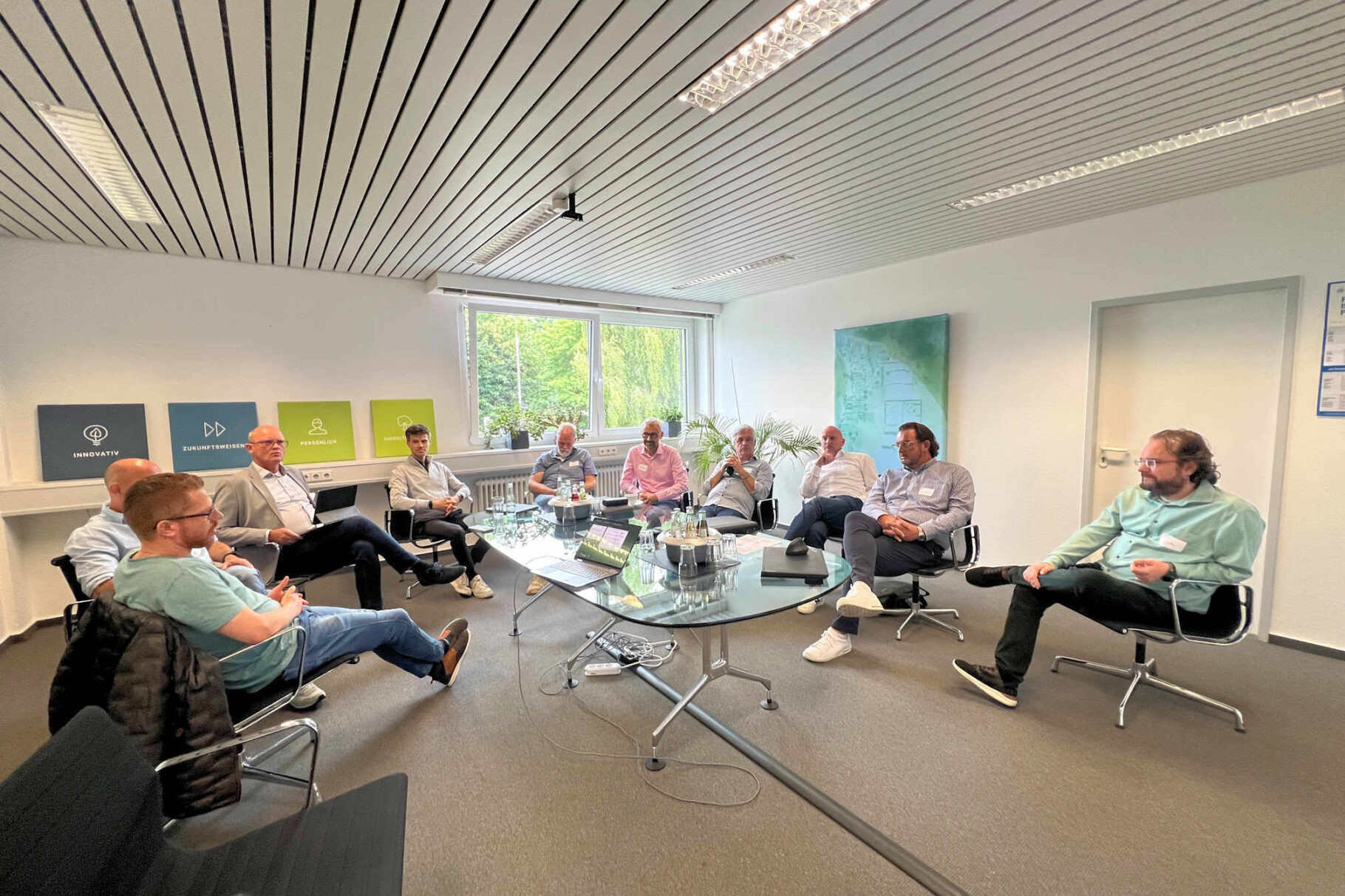 Teilnehmer um einen ovalen Tisch sitzend.