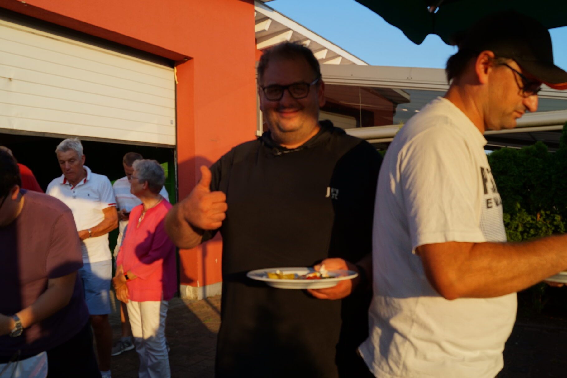 ein Mann zeigt einen Daumen hoch und hält einen Teller mit Grillzeug in die Höhe