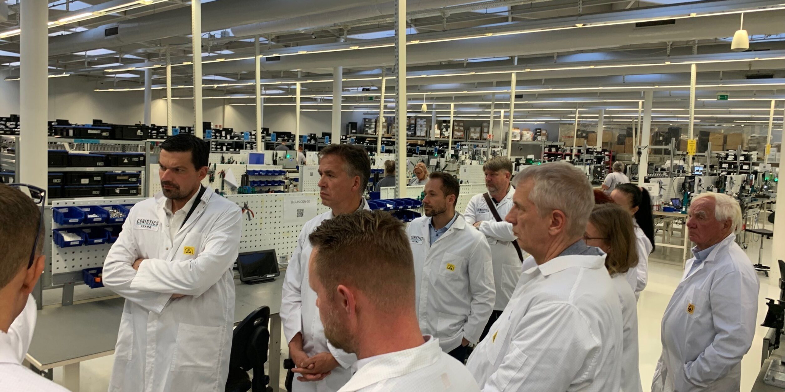 Unternehmer*innen besichtigen ein Werk und tragen dabei weiße Kittel