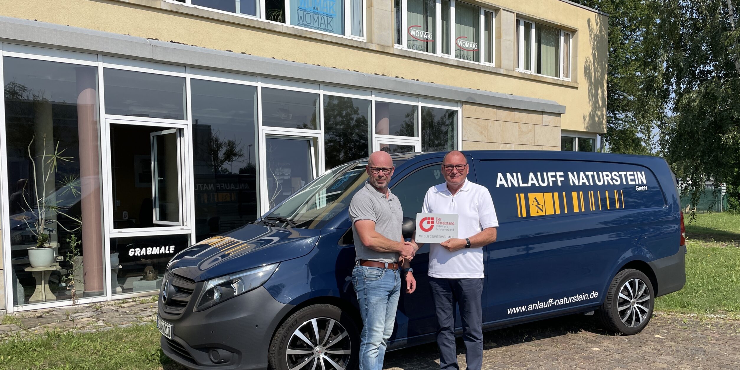 zwei Männer stehen vor einem Firmentransporter und reichen sich die Hände