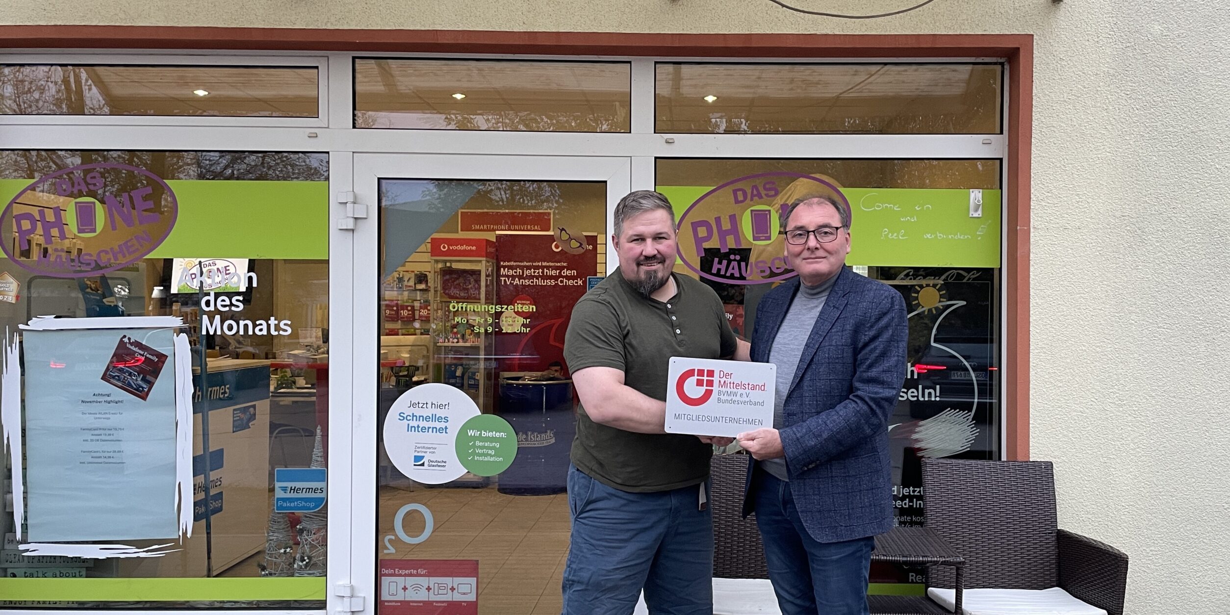 zwei Männer stehen vor einem Telefonladen und halten ein Schild in der Hand
