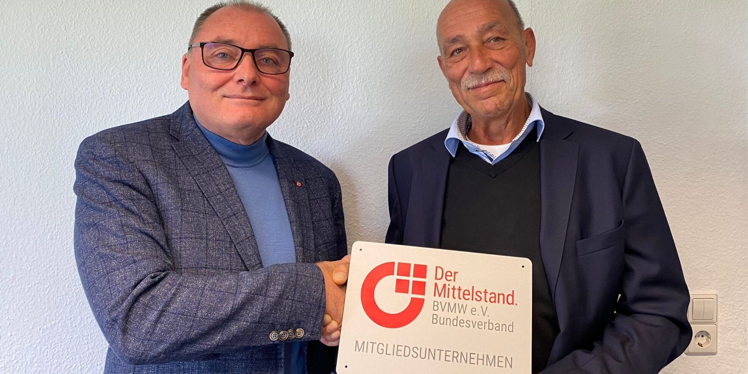 zwei Männer schütteln sich die Hände und halten ein Schild in die Höhe