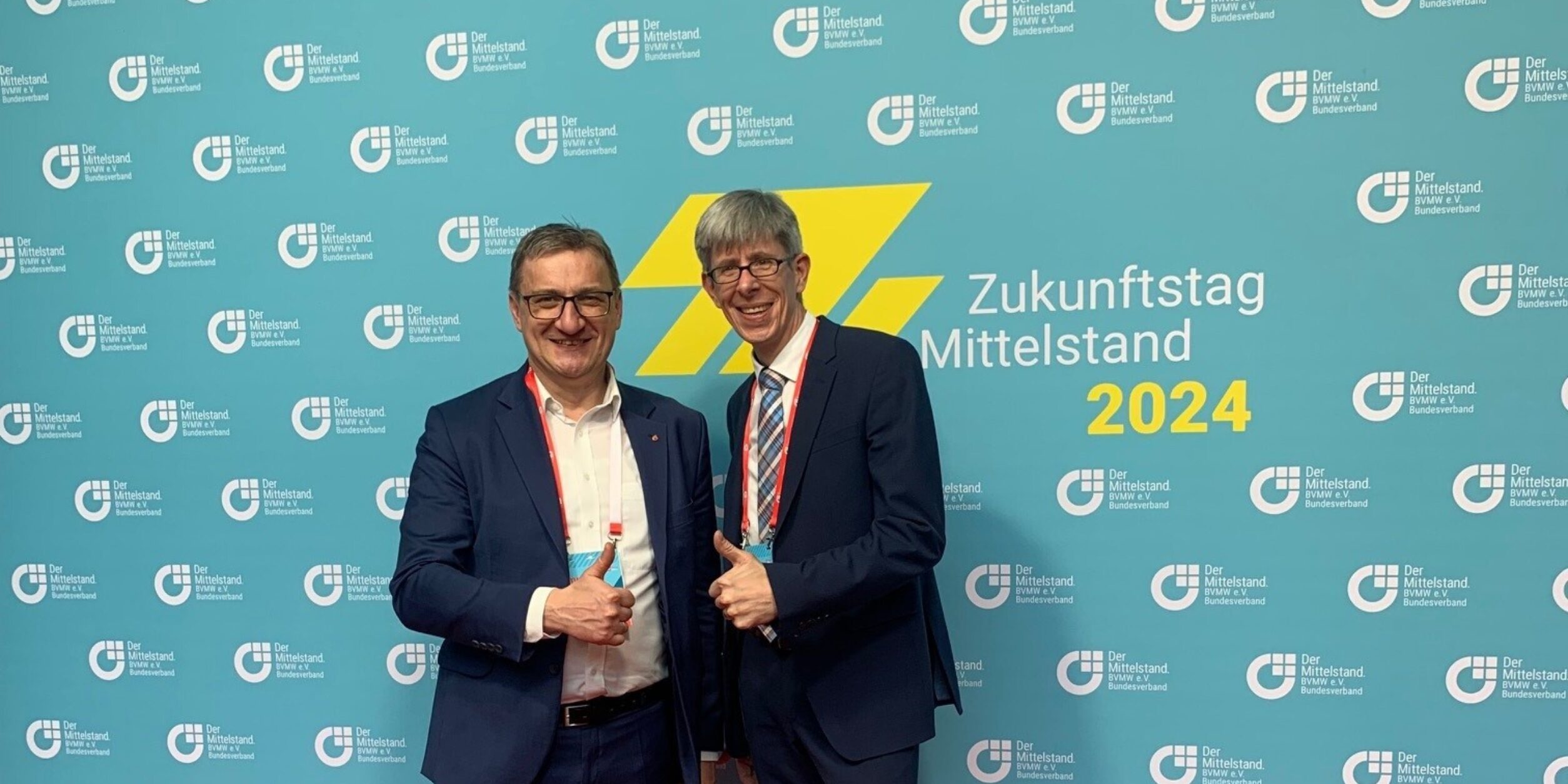 zwei Männer stehen vor einer Imagewand und zeigen Ihre Daumen nach oben