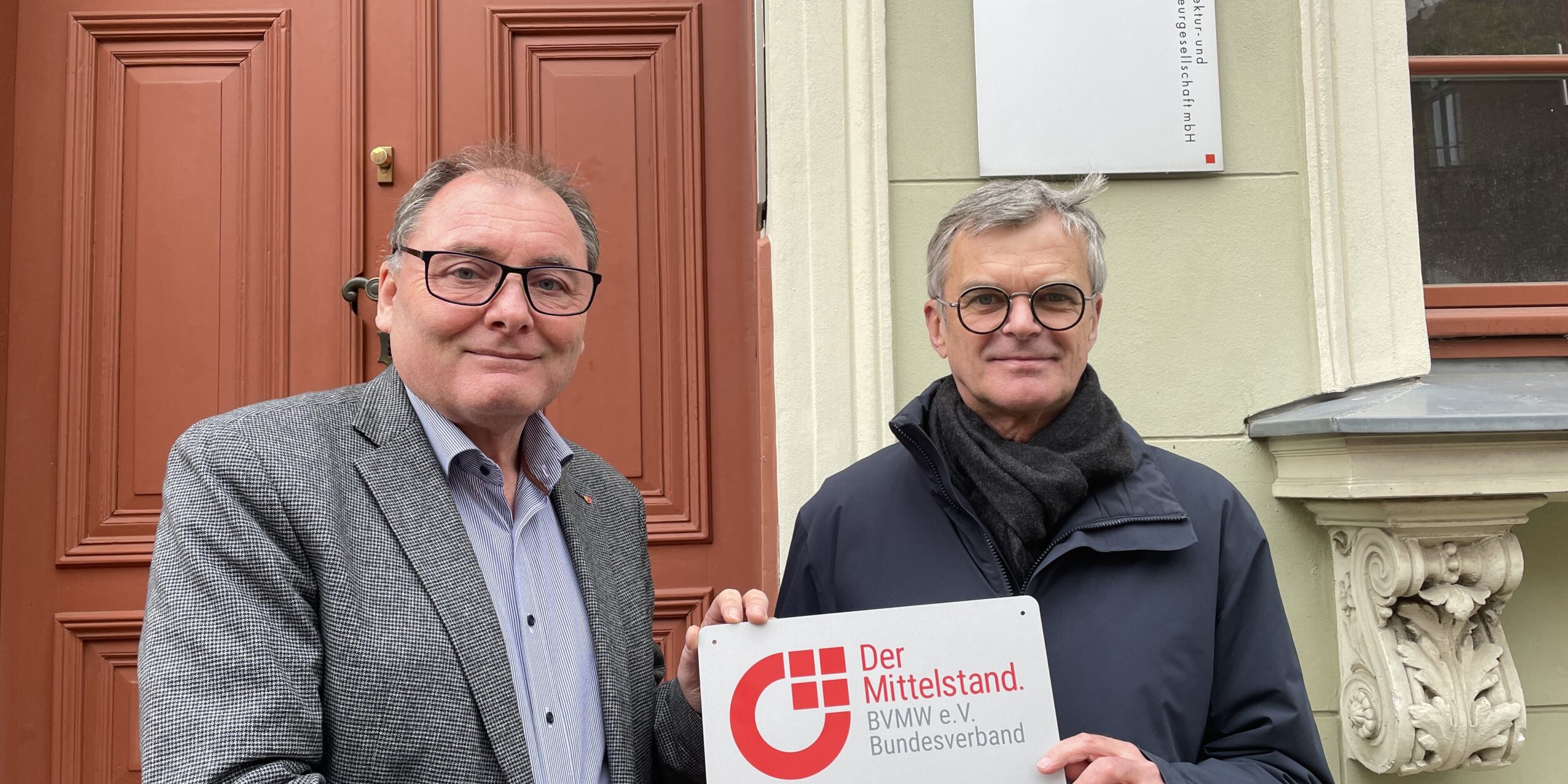 Zwei Männer stehen vor einem Gebäude und halten ein Schild in die Höhe