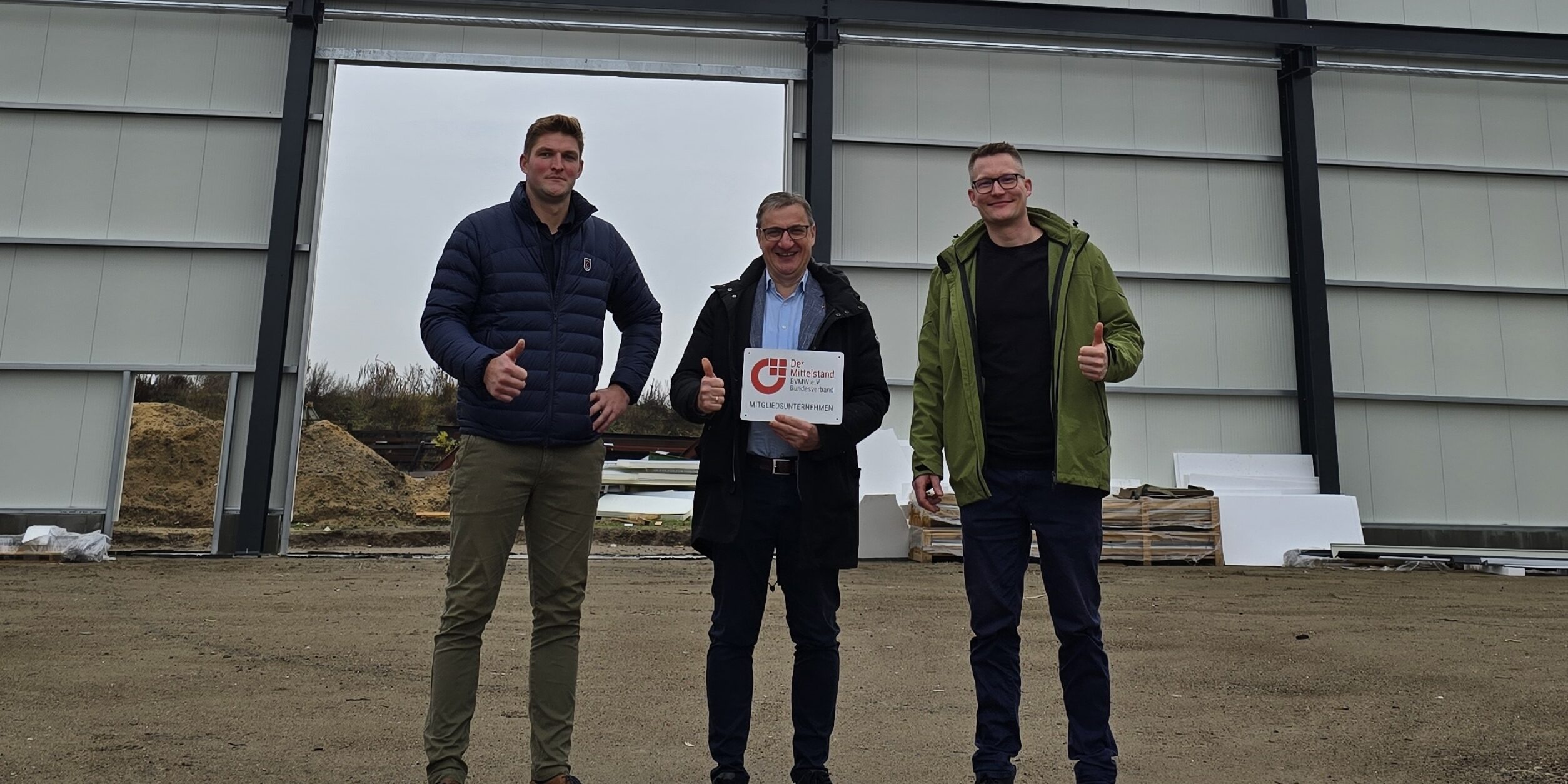 Drei Männer stehen in einer Halle uns halten ein Schild in die Höhe