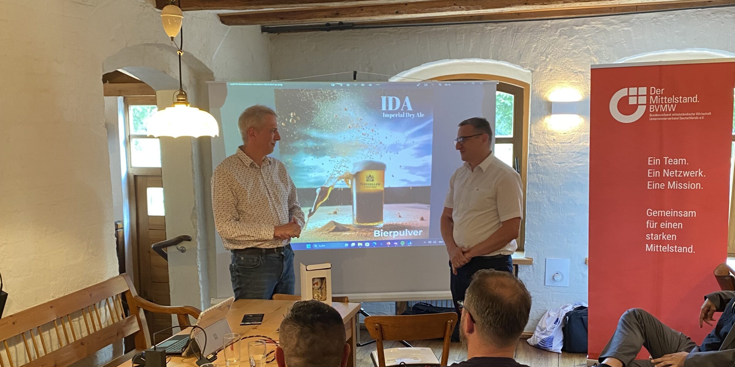 Zwei Männer begrüßen Unternehmer*innen zum Vortrag