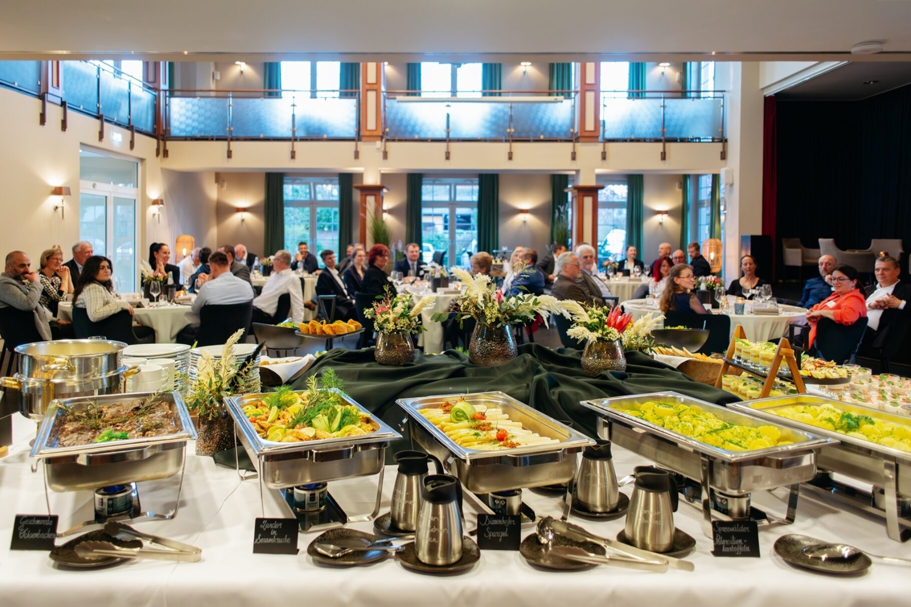 Regionales Buffet im Vordergrund. Im Hintergrund Teilnehmer der Veranstaltung