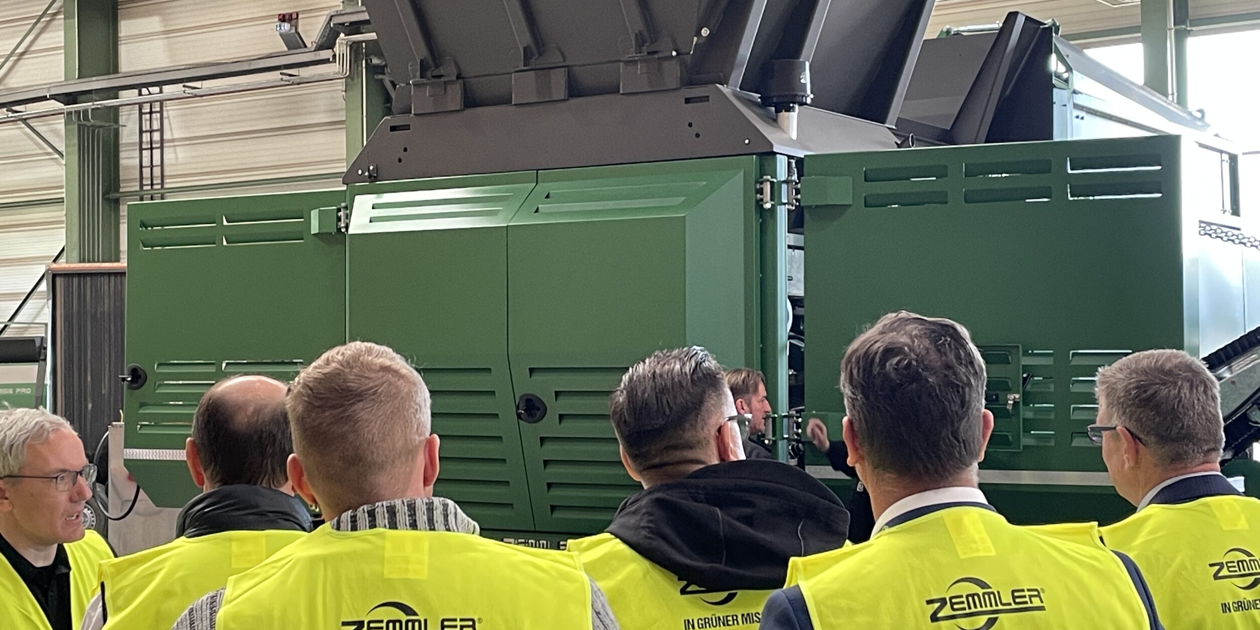 Teilnehmer mit neongelben Warnwesten von Zemmler Siebanlagen in der Fertigungshalle. Im Hintergrund MULTI SCREEN Siebanlage.