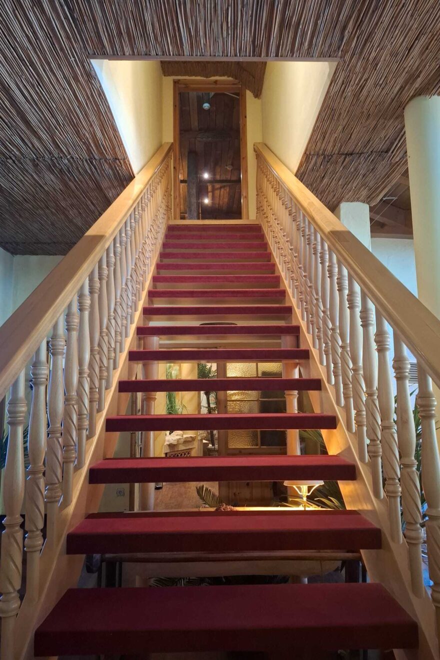 Eine steile Holztreppe im Wellnesshotel Seeschlösschen, welche mit rotem Samt bezogene Treppenstufen hat.