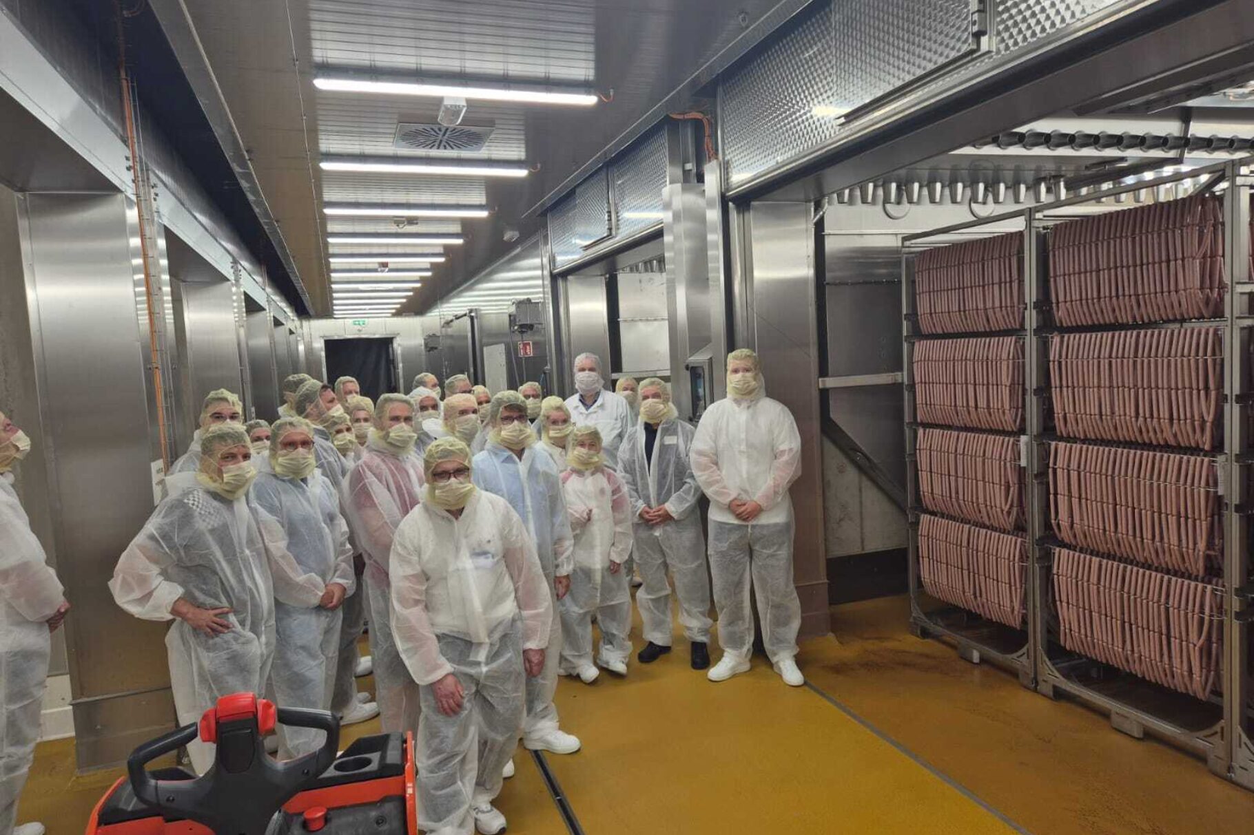 links im Bild: Teilnehmer der Veranstaltung in Hygienebekleidung, rechts im Bild: 1 von 8 Räucherkammern mit 350 000 Würsten