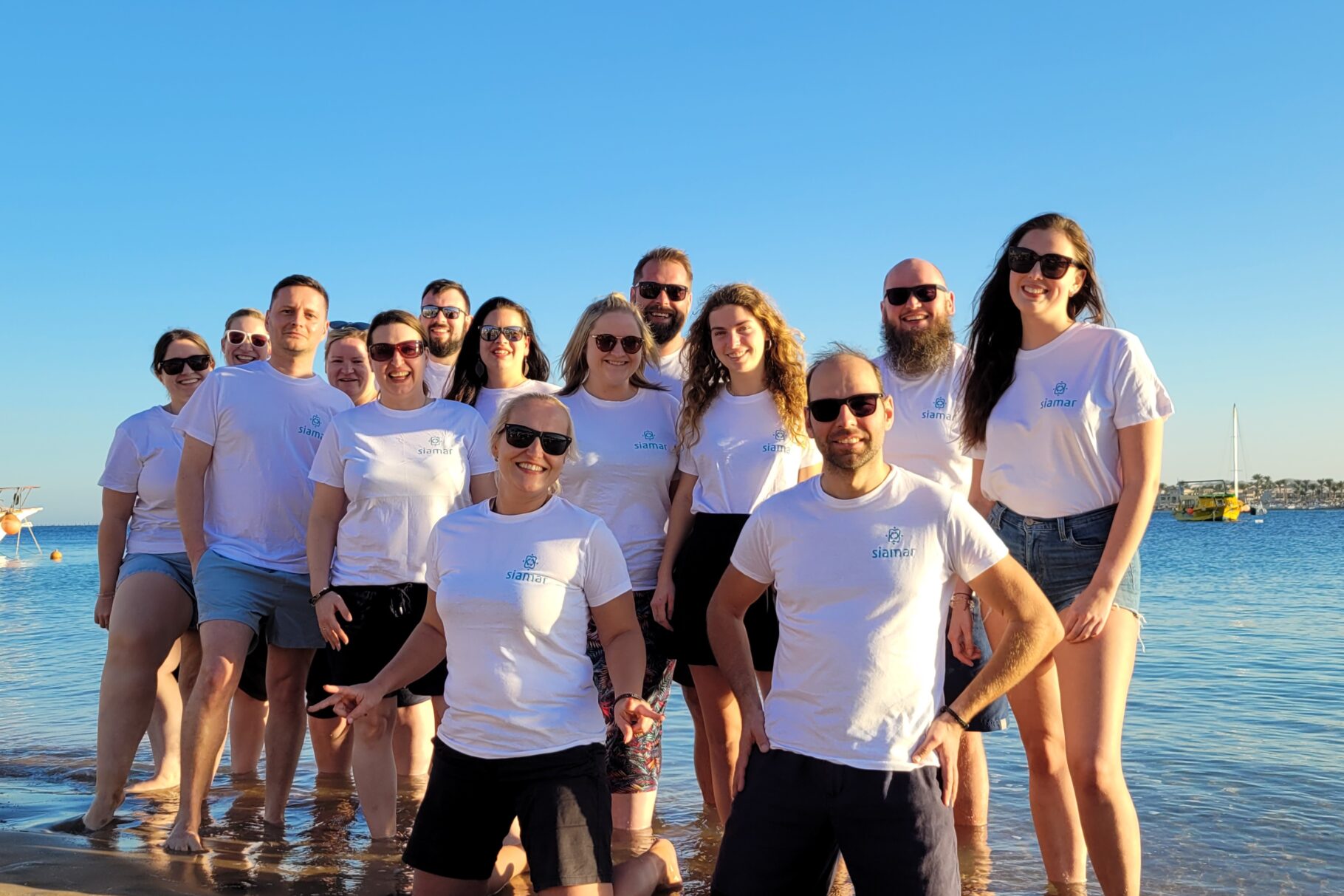 Mitarbeitende von Siamar Reisen im weißen Tshirt am Strand im Hintergrund Meer