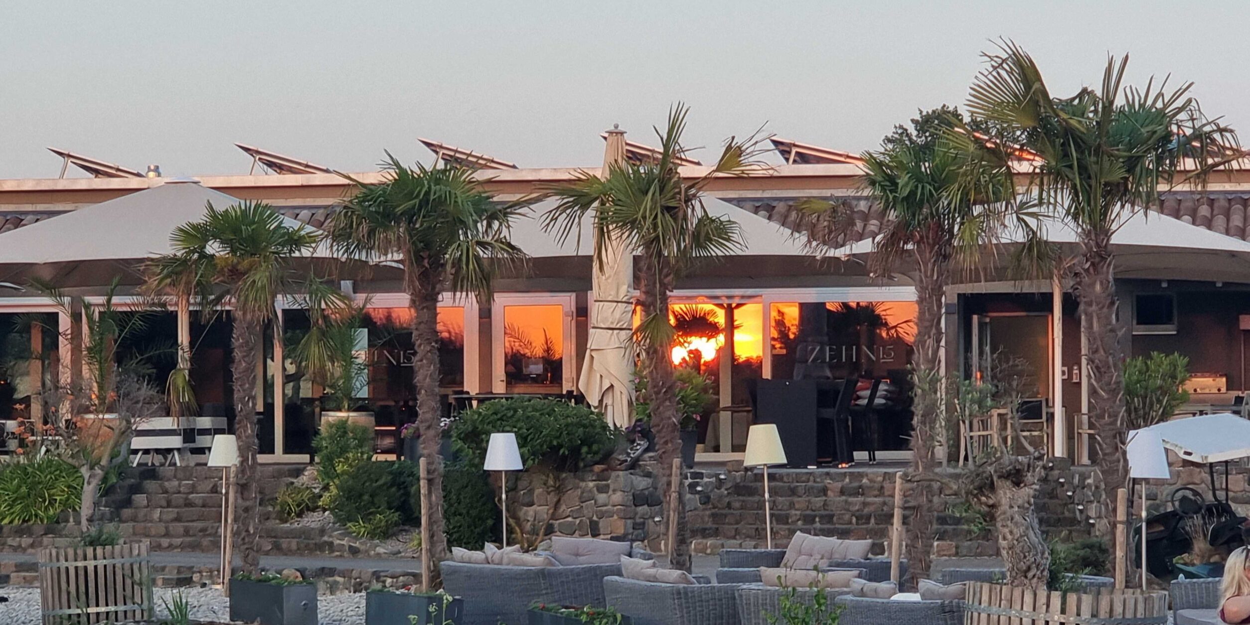 Außenbereich vom Golf Club Machern mit Sitzgelegenheiten, großen Sonnenschirmen und großen Palmen