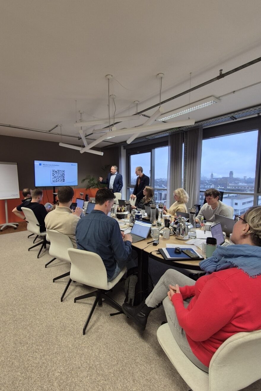 Workshop-Teilnehmende sitzen mit ihren Laptops zusammen an einem großen Tisch